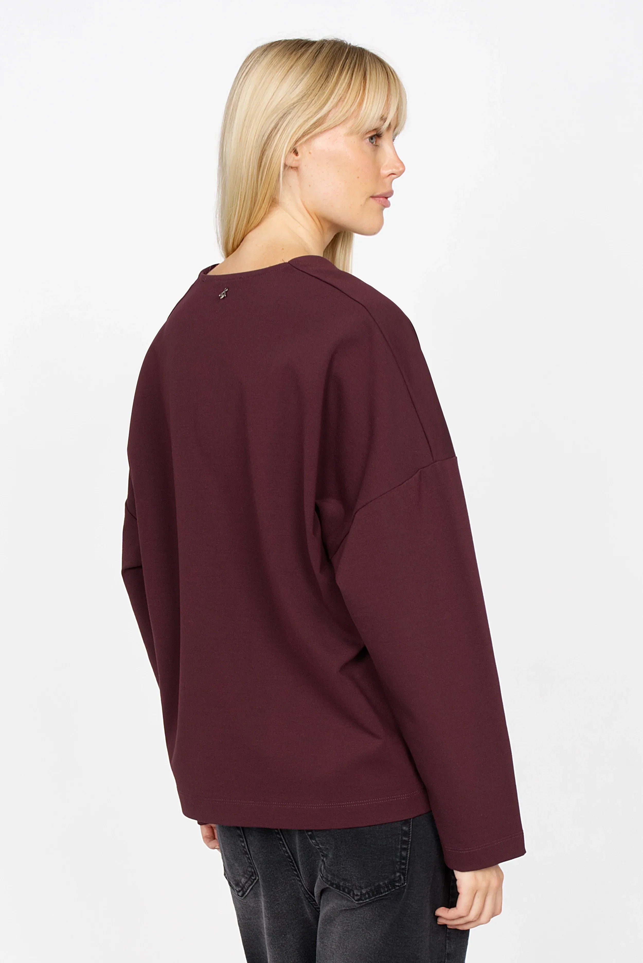 Damen trägt BERLEY Relaxed V-Neck Bluse in dunklem Bordeauxrot aus weichem, knitterfreiem Jersey mit überschnittenen Schultern und lässiger Passform, Rückansicht.