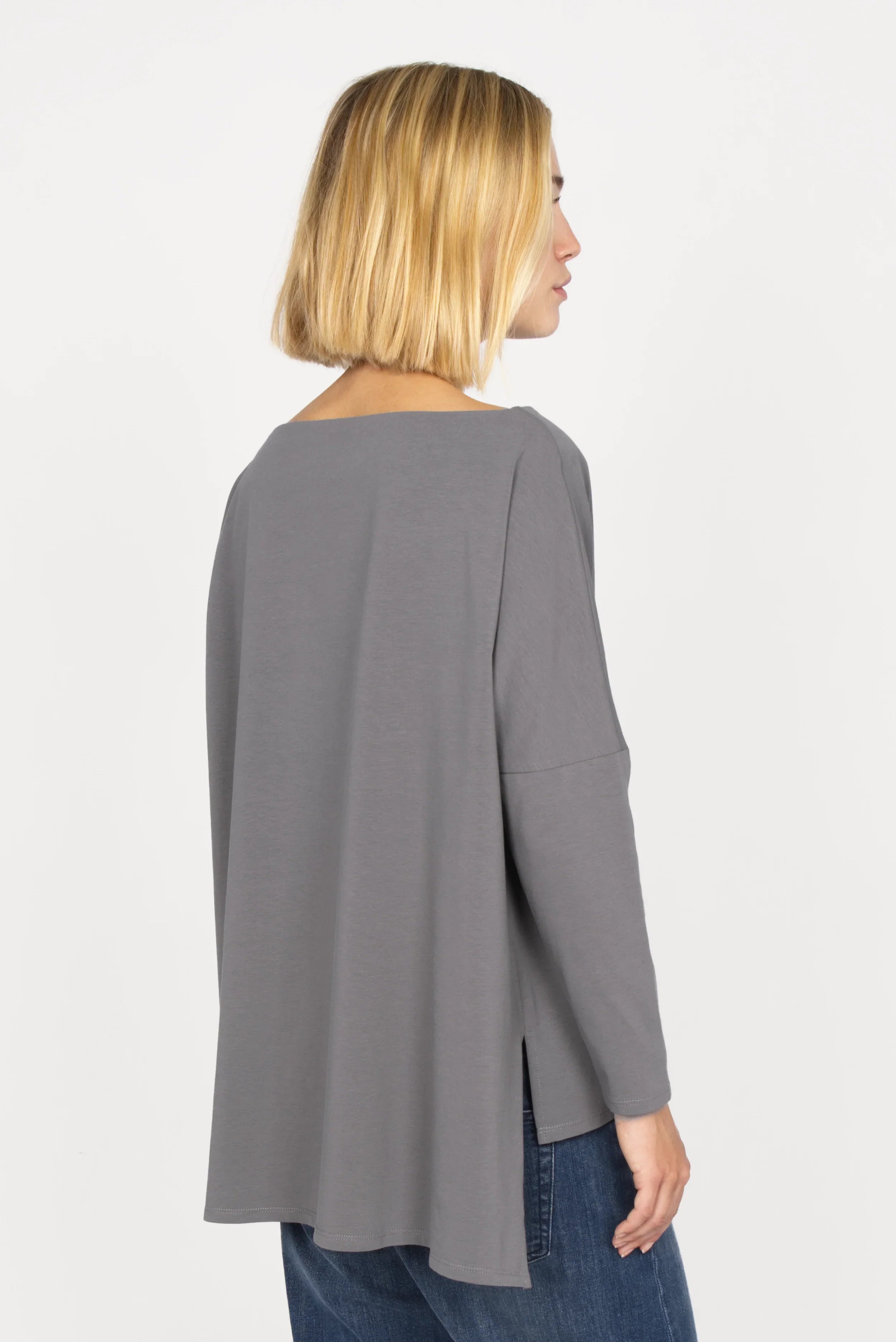 Back view of a model wearing gray AMALEA Relaxed Fit Longsleeve with boat neckline, dropped shoulders, side slits, and a longer back hem