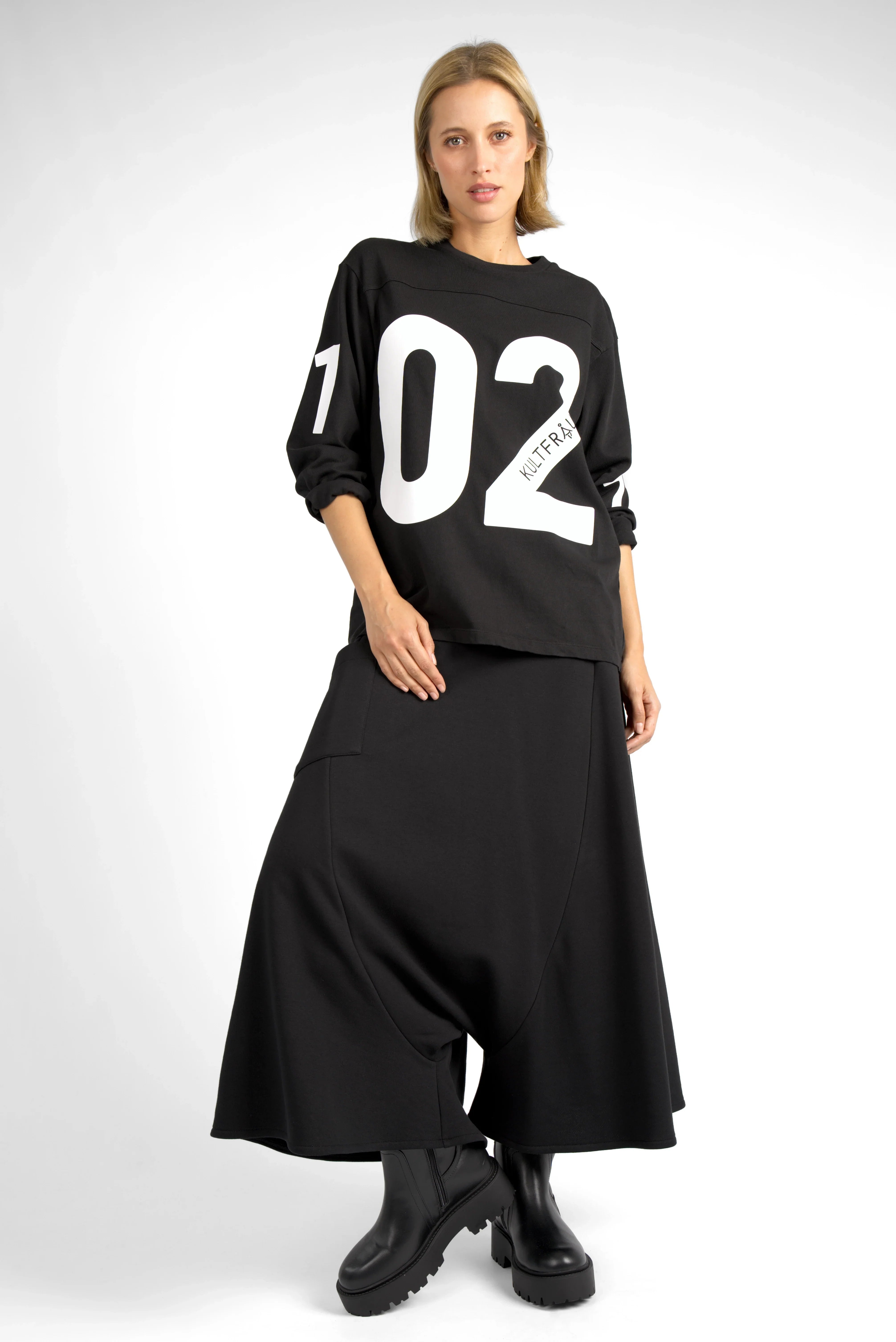 Woman wearing black AGA Statement Sweater with bold white number print and black skirt