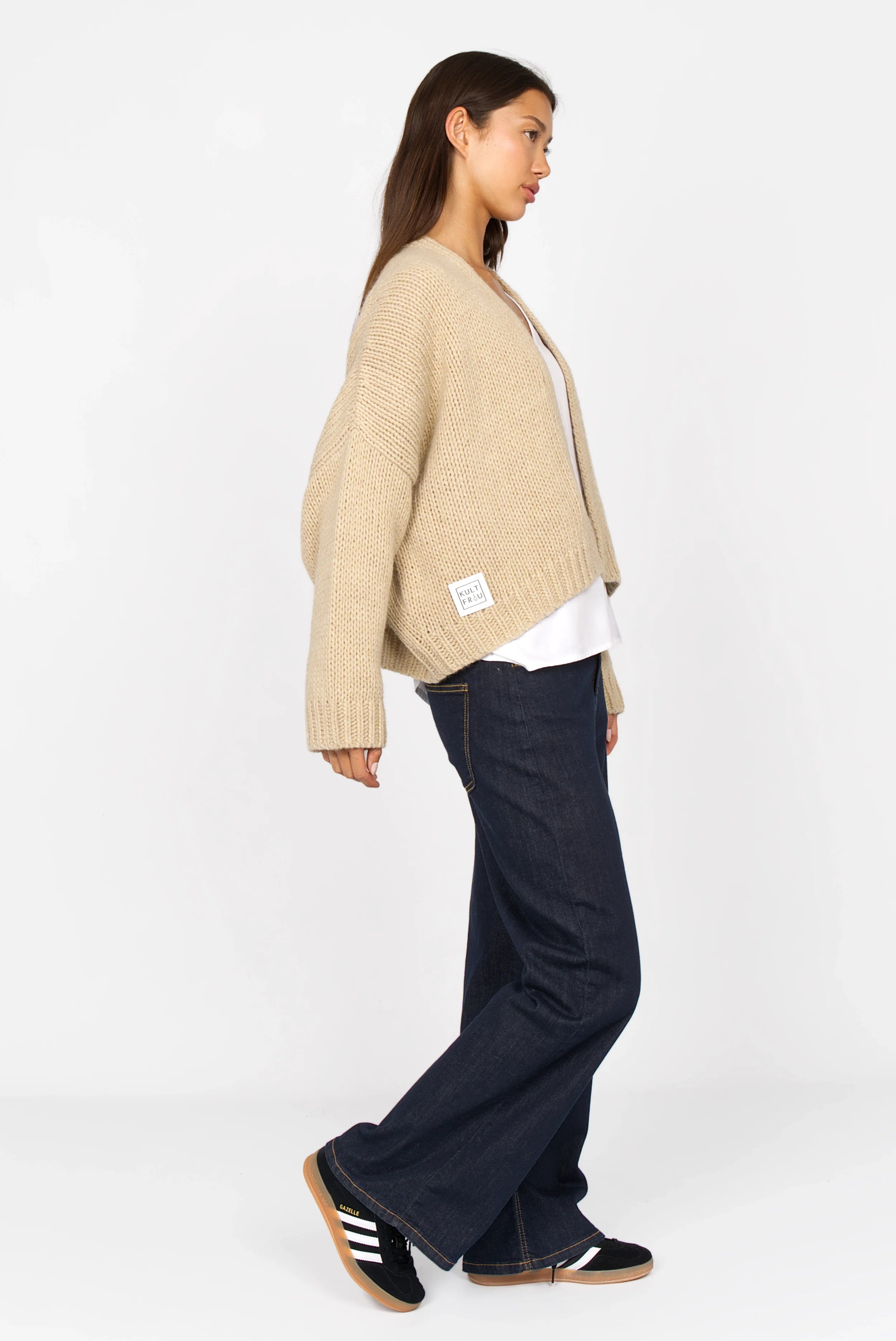 Woman wearing beige ALIXA cropped knit cardigan with shawl collar and oversized fit paired with dark wide-leg jeans and black sneakers