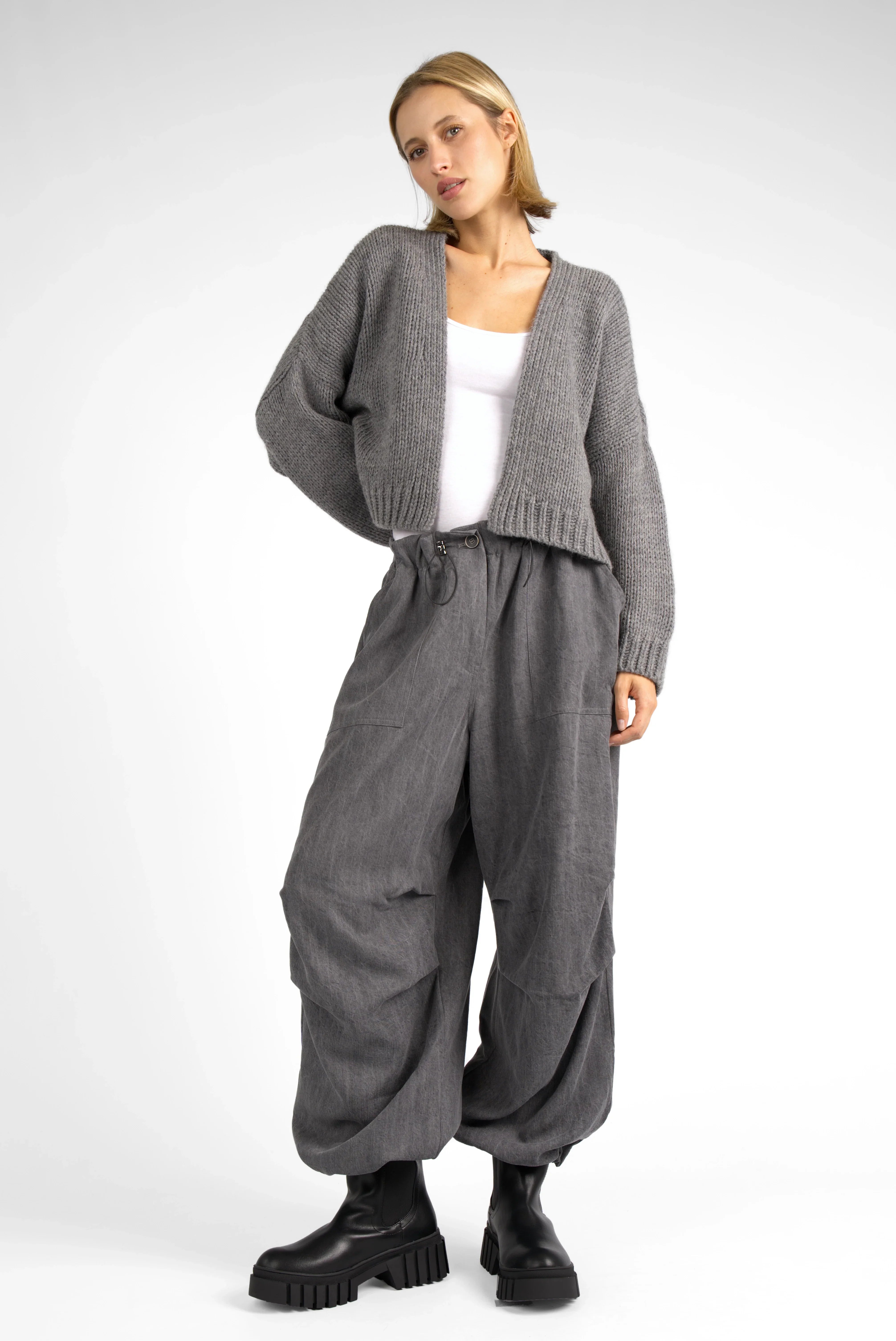 Woman wearing grey ALIXA Cropped Strickcardigan with loose fit, shawl collar, and ribbed cuffs paired with wide-leg pants and black boots.