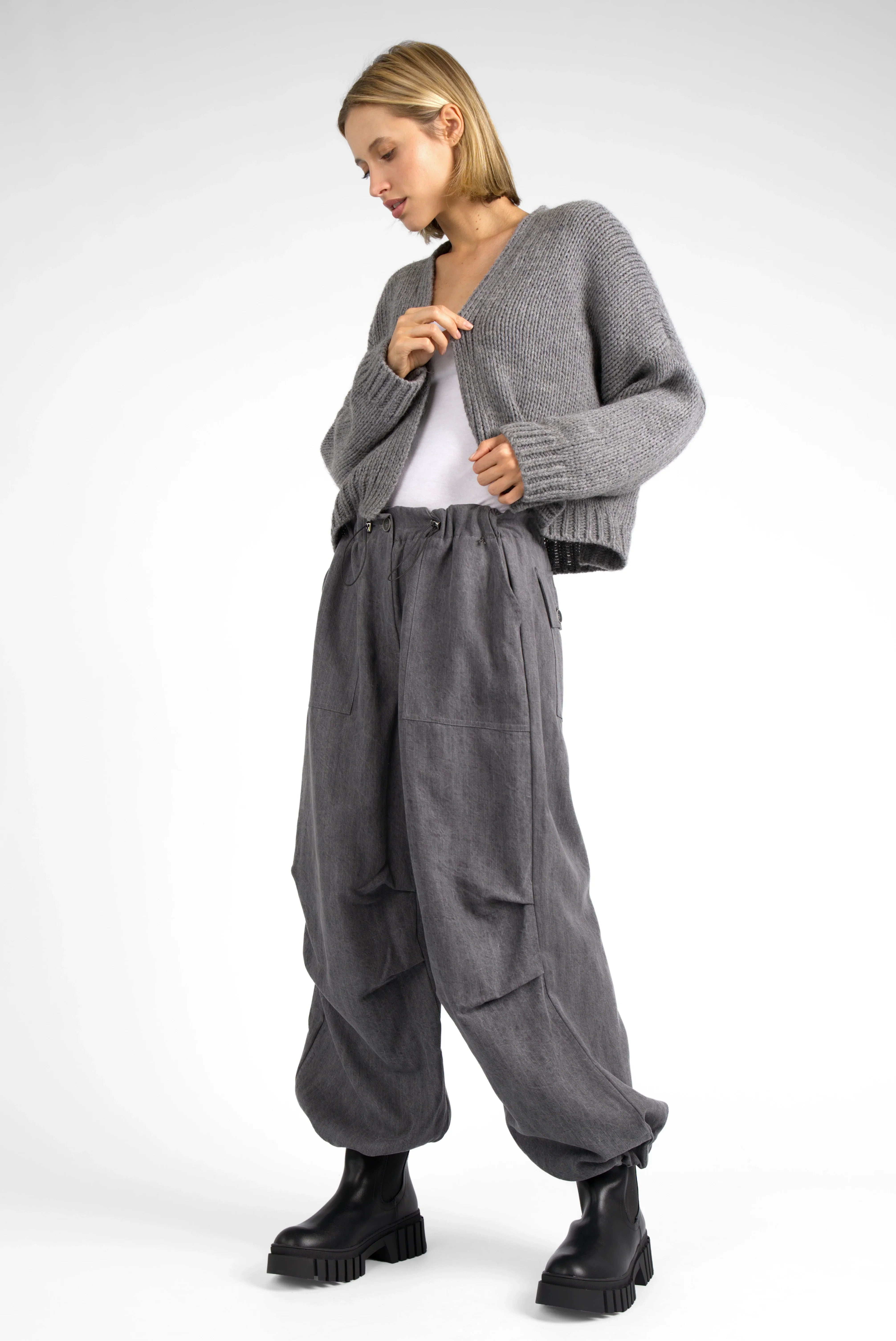 Woman wearing ALIXA cropped grey knit cardigan with loose fit and ribbed cuffs paired with baggy grey pants and black boots