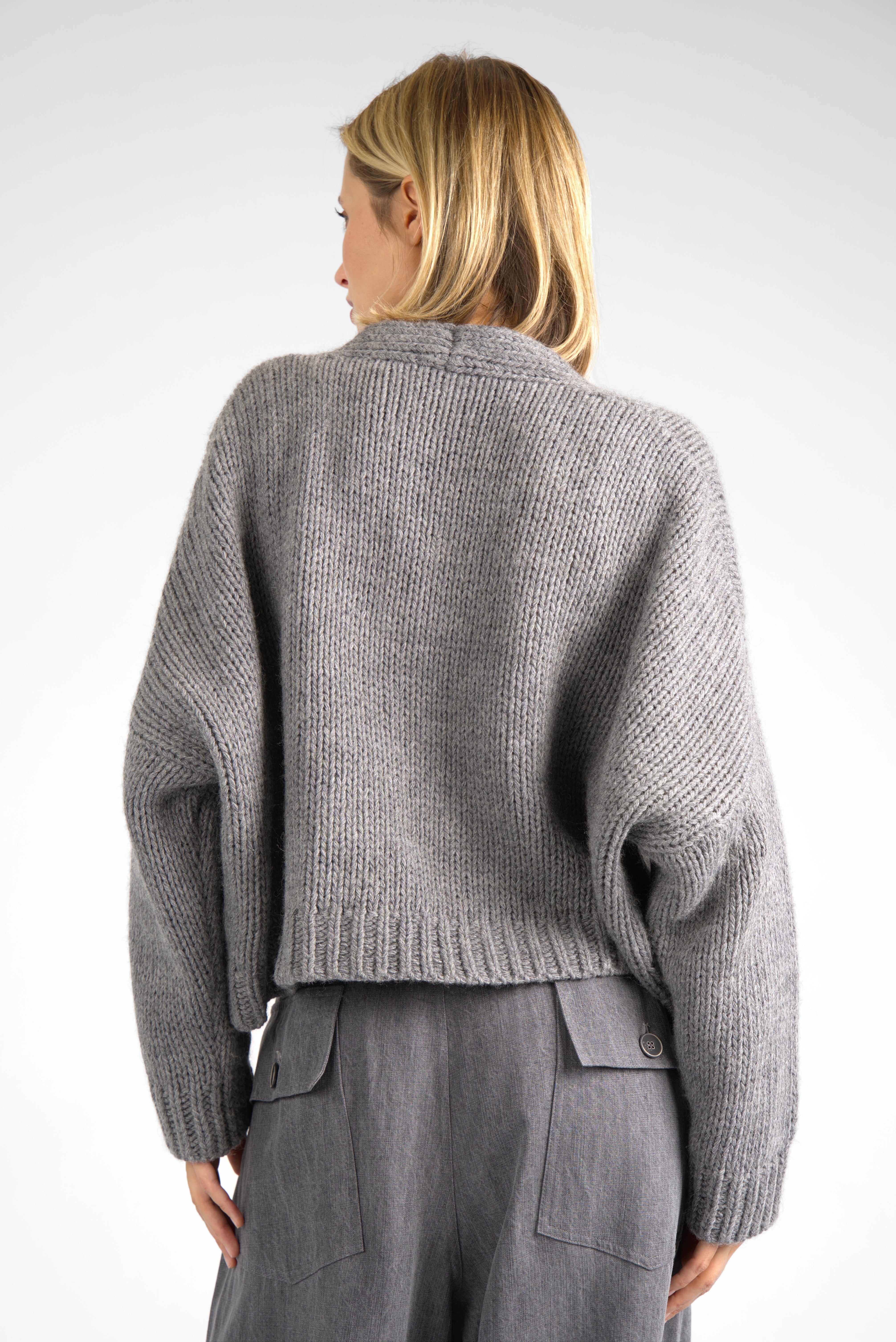 Back view of a woman wearing a grey ALIXA Cropped Strickcardigan with loose fit and dropped shoulders.