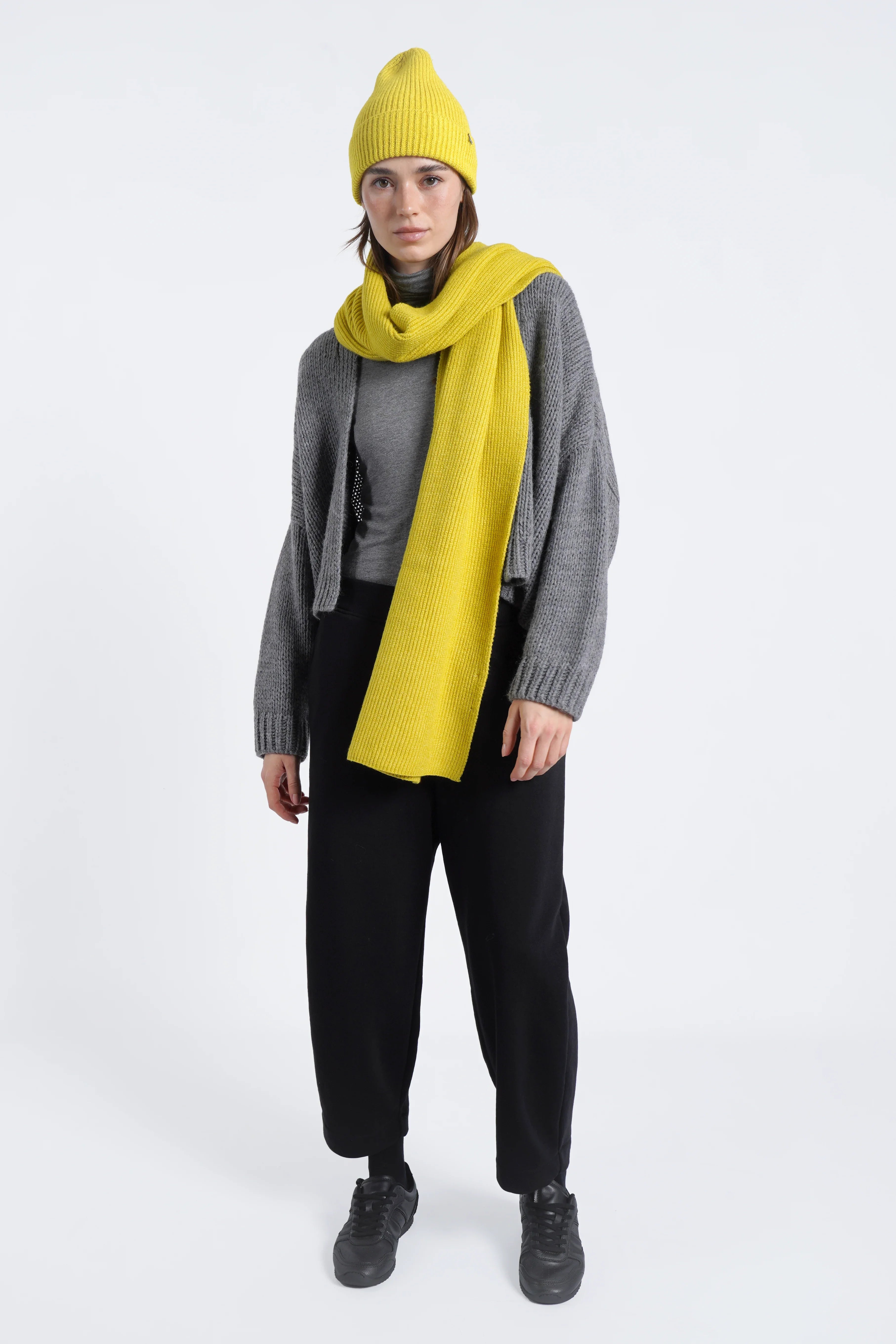 Frau trägt gelben gerippten Schal aus weichem Viskose-Mix kombiniert mit grauer Strickjacke und schwarzer Hose