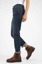 Dark blue boyfriend-jeans with relaxed fit, mid waist, and destroyed details, styled cuffed with brown boots.