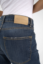 Dark blue boyfriend jeans with mid waist and relaxed fit, featuring destroyed details and a leather brand patch on the back waistband.