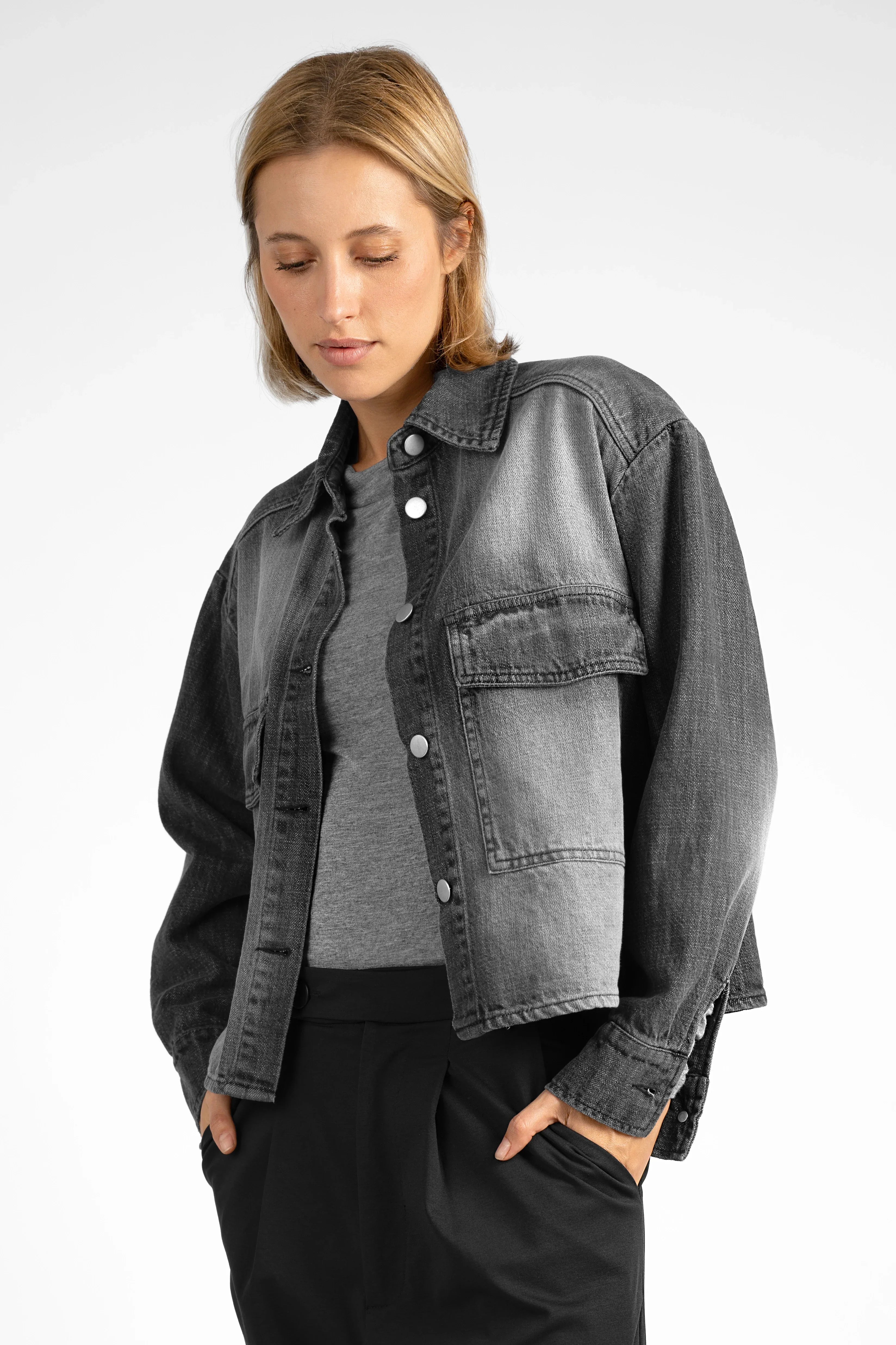 Frau trägt AMAKU Revive Hemdjacke in schwarzer kurzer Denim-Optik mit aufgesetzten Brusttaschen und Regular Fit