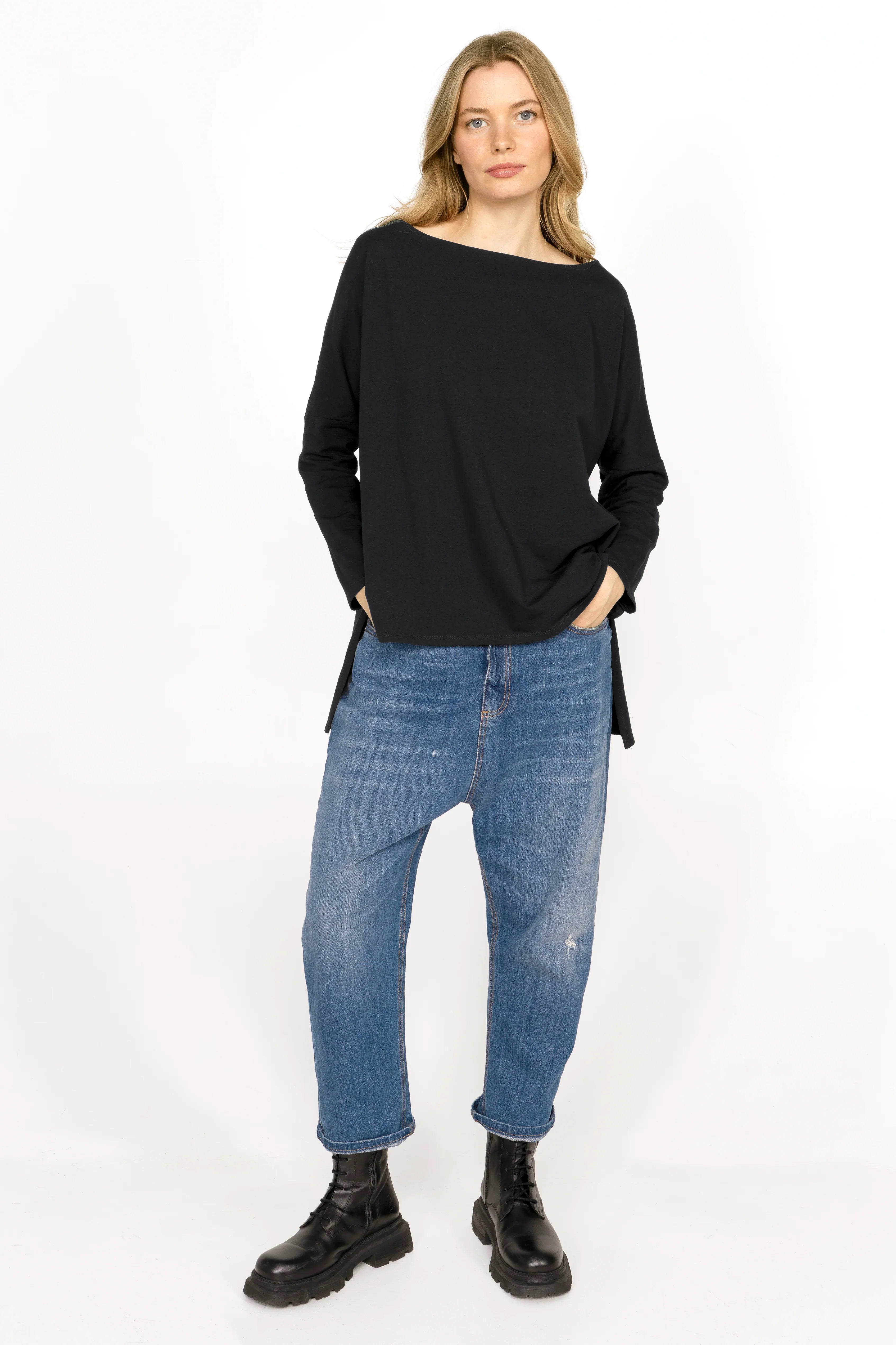 Woman wearing black AMALEA Relaxed Fit Longsleeve with boat neckline, dropped shoulders, side slits, and longer back hem paired with blue jeans and black boots