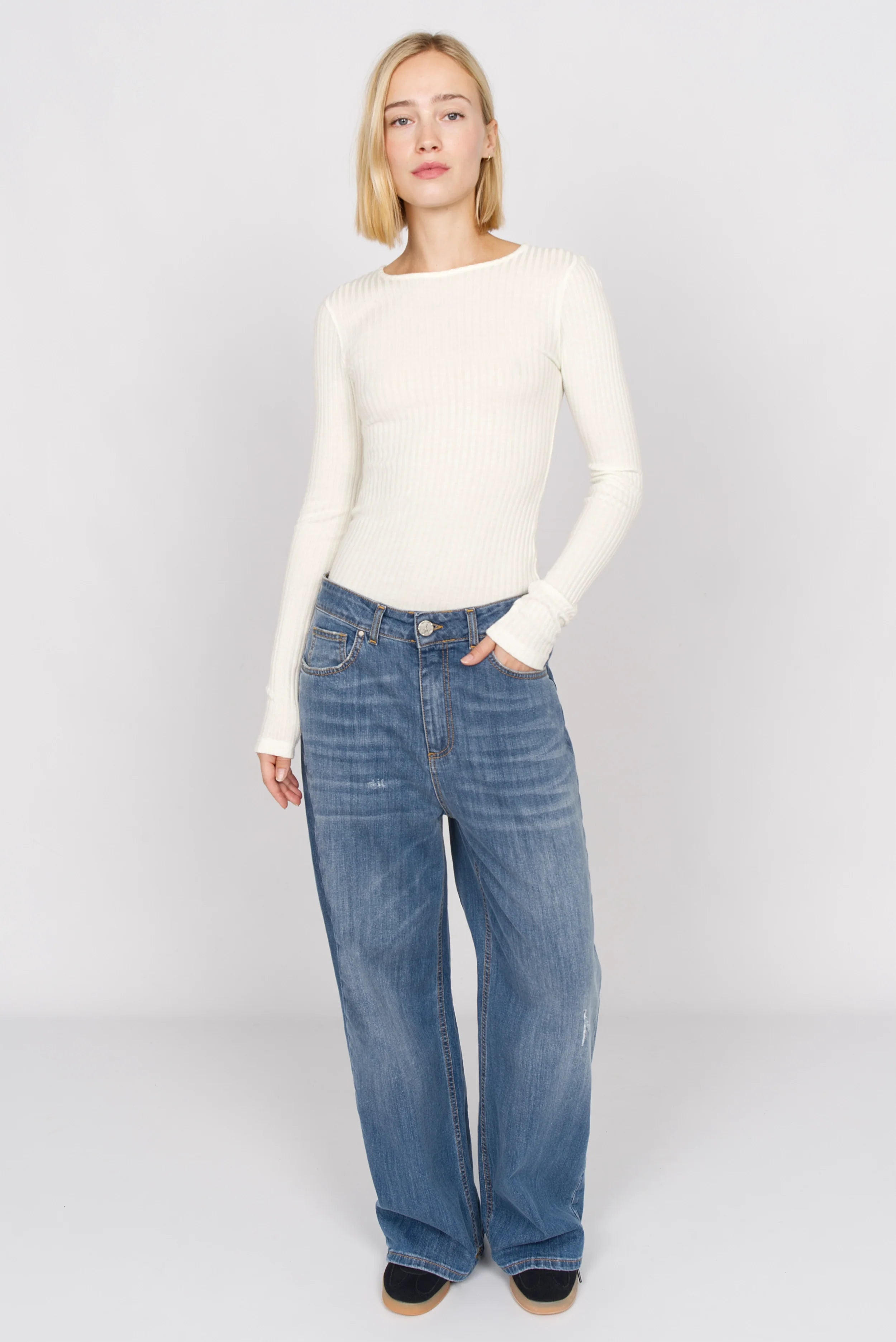 Woman wearing white BETTIE Longsleeve slim fit ribbed knit top with extra long sleeves and round neckline paired with blue wide-leg jeans