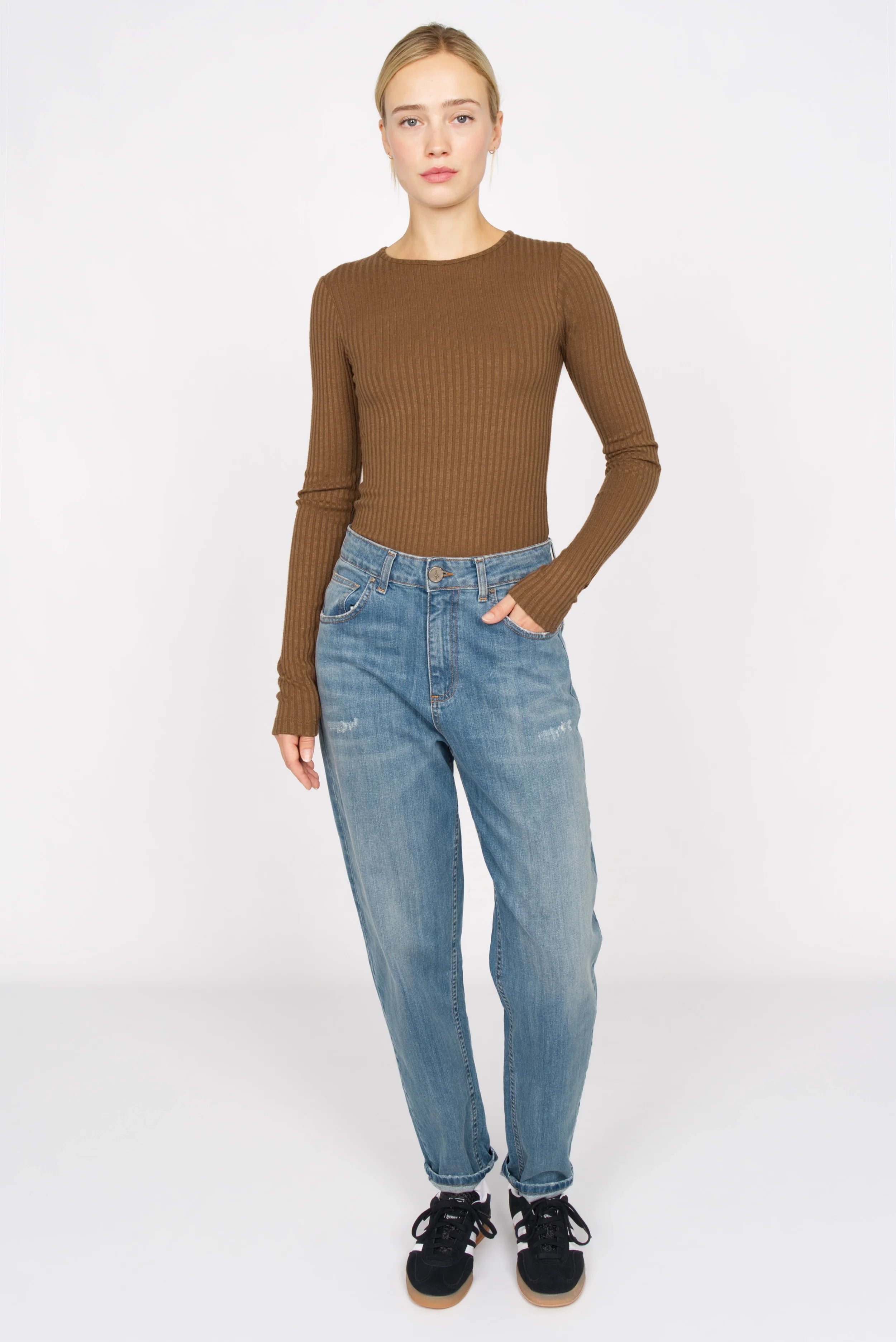 Model wearing brown Bettie Longsleeve ribbed slim fit top with long sleeves and round neckline paired with blue jeans and black sneakers