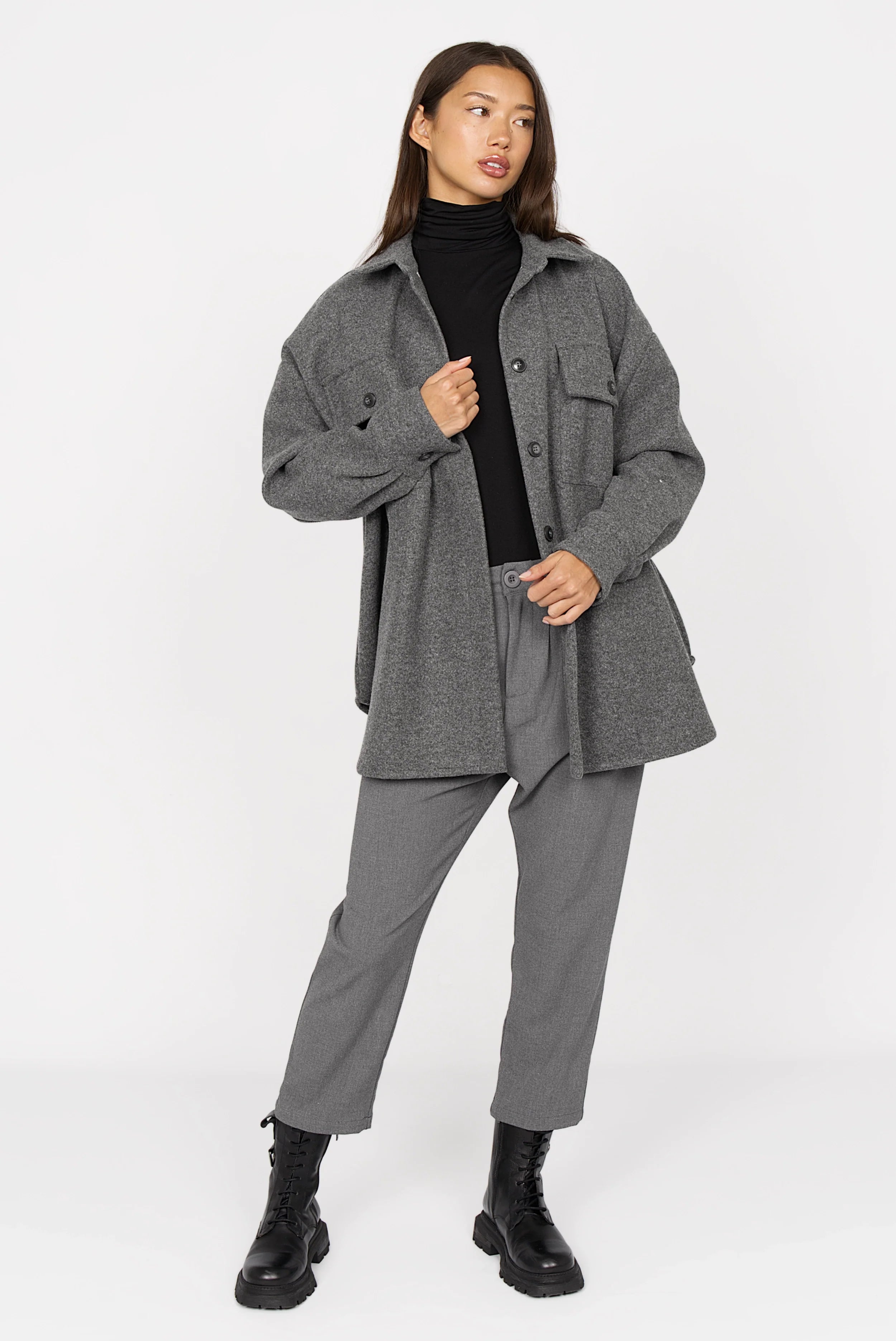 Woman wearing grey BJORA Overshirt made of wool blend with chest pockets and side pockets, styled over black turtleneck and grey pants
