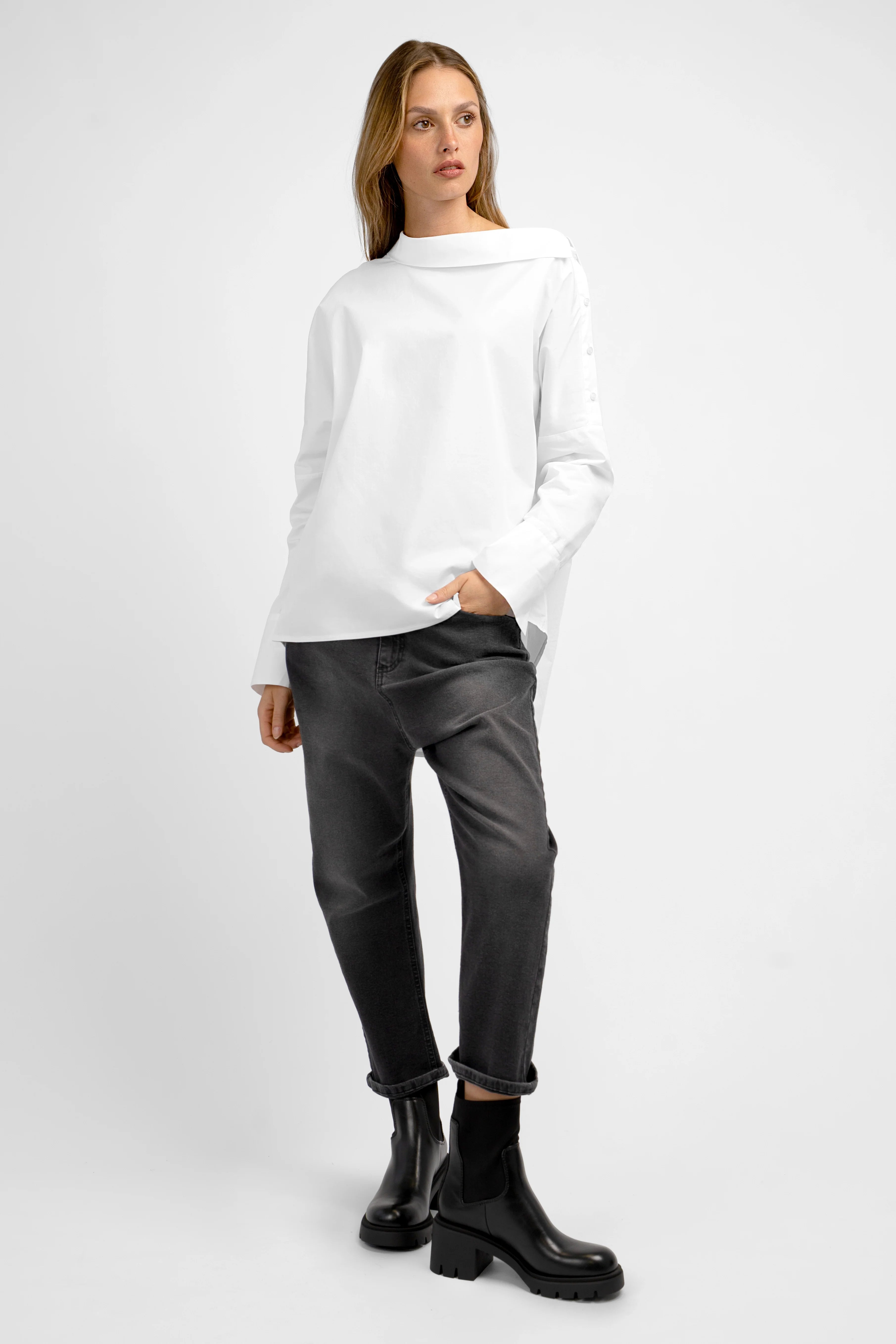 Frau trägt weiße BONI Asymmetrische One Shoulder Bluse mit Knopfleiste und schwarzer Hose.