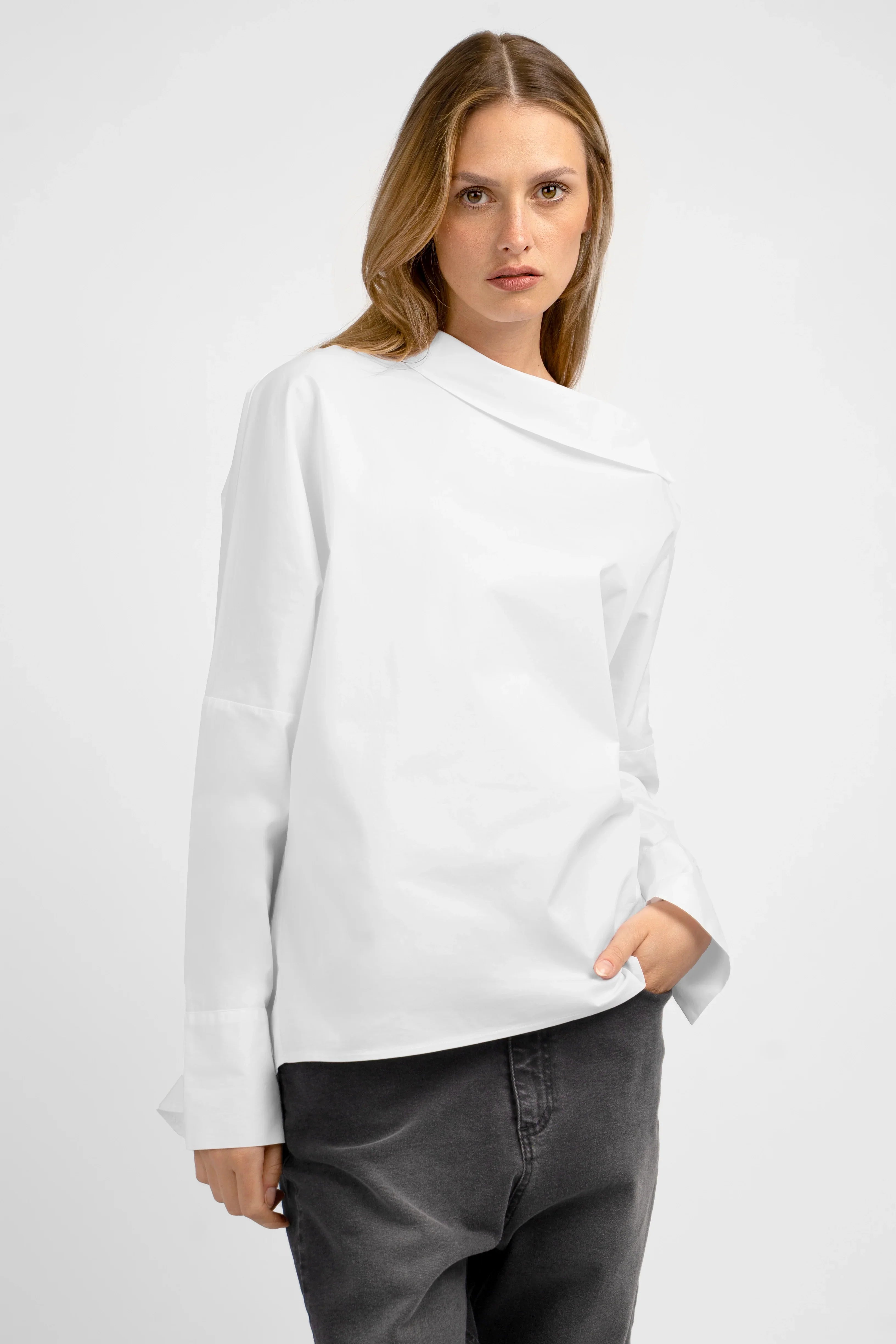 Frau trägt weiße BONI asymmetrische One Shoulder Bluse mit breiten Manschetten und verlängertem Rücken