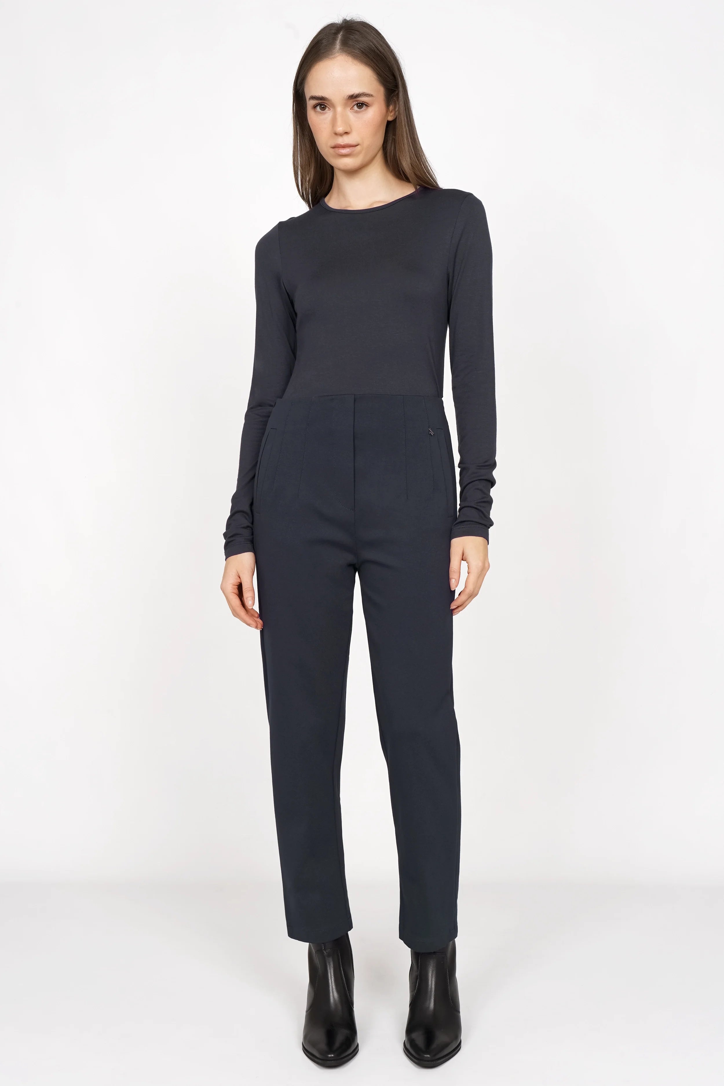 Female model wearing black CEELIA ankle pants with a slim fit and cropped length, paired with a long-sleeve black top and black ankle boots.