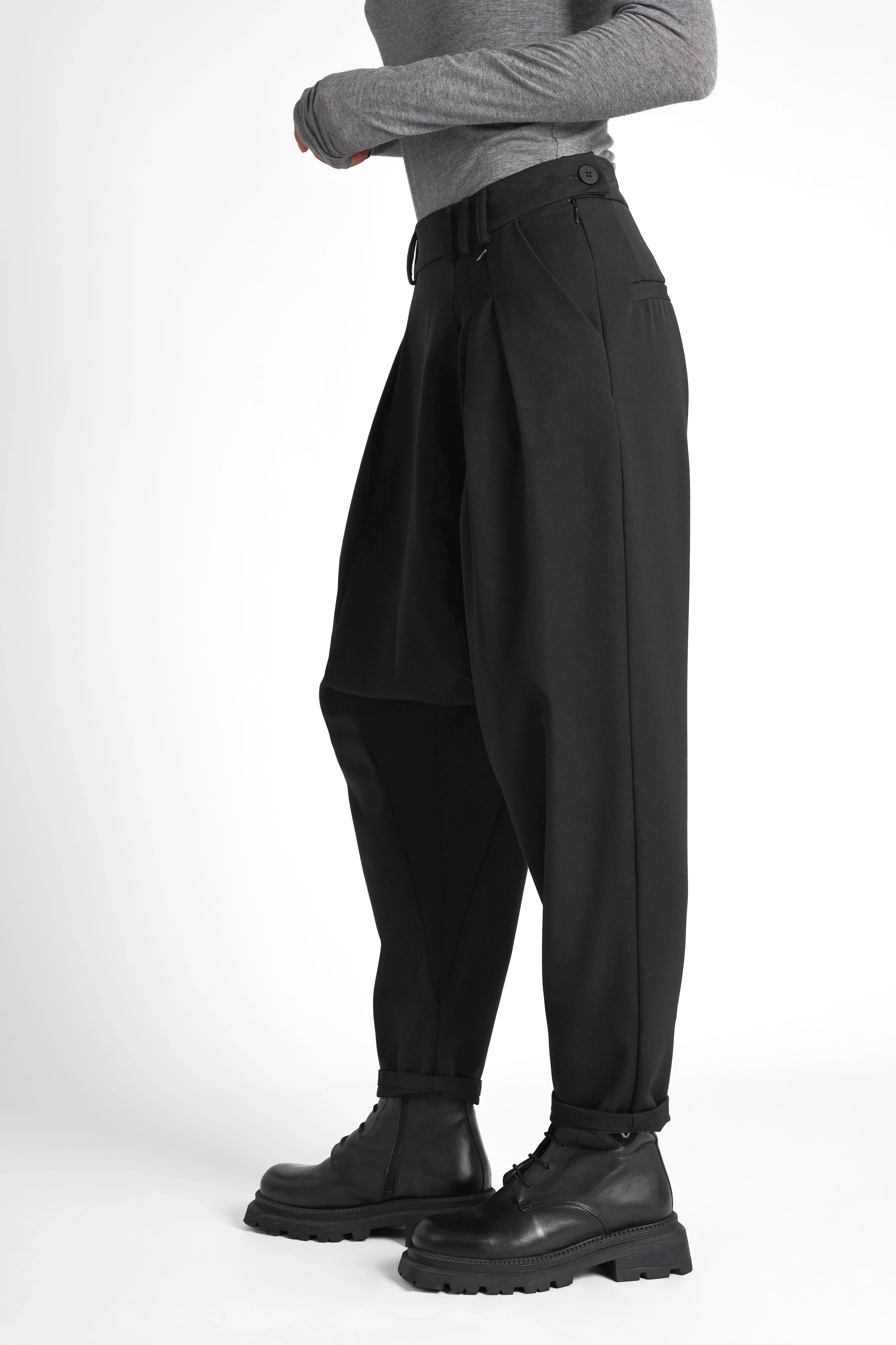 Schwarze DEEP Avantgarde-Hose mit extra tiefem Schritt, seitlicher Knopfschließe, Bundfalten und tapered leg, kombiniert mit soften Materialien und relaxed fit.