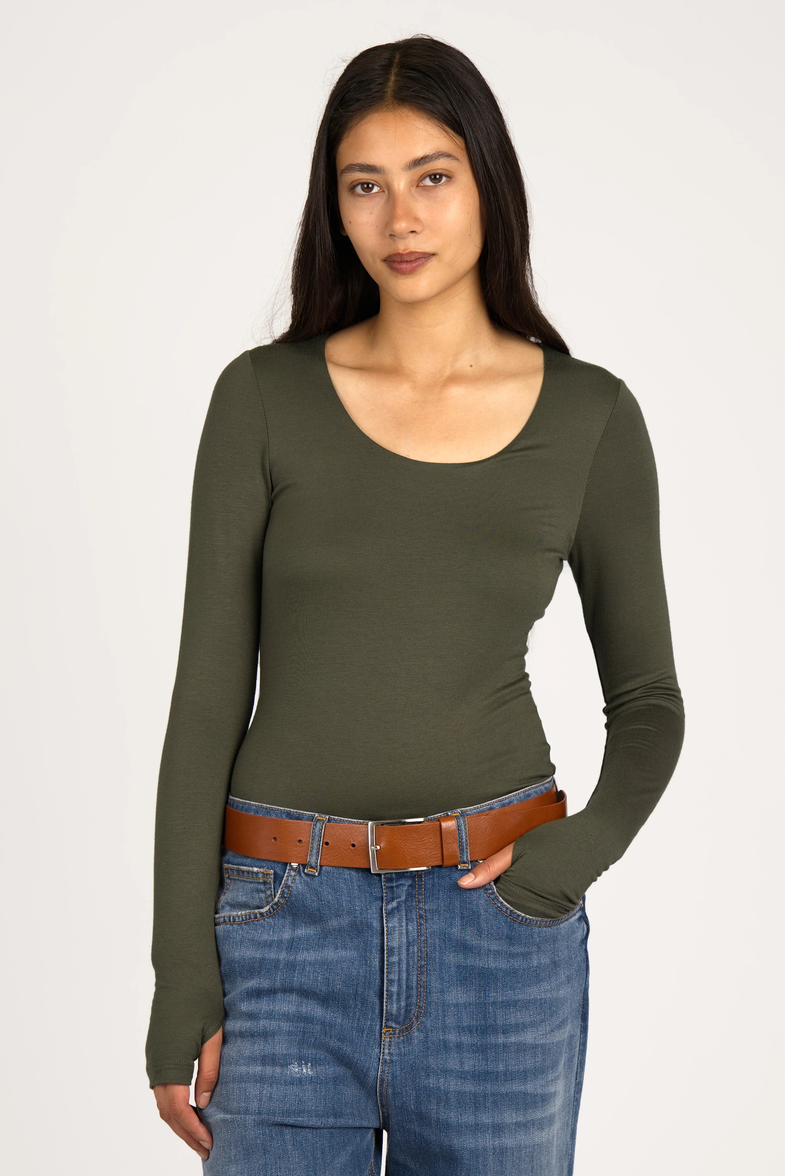 Frau trägt olivegrünes VALUM Longsleeve mit U-Boot-Ausschnitt, extra langen Ärmeln und Daumenlöchern in Slim Fit zu Jeans und braunem Gürtel.