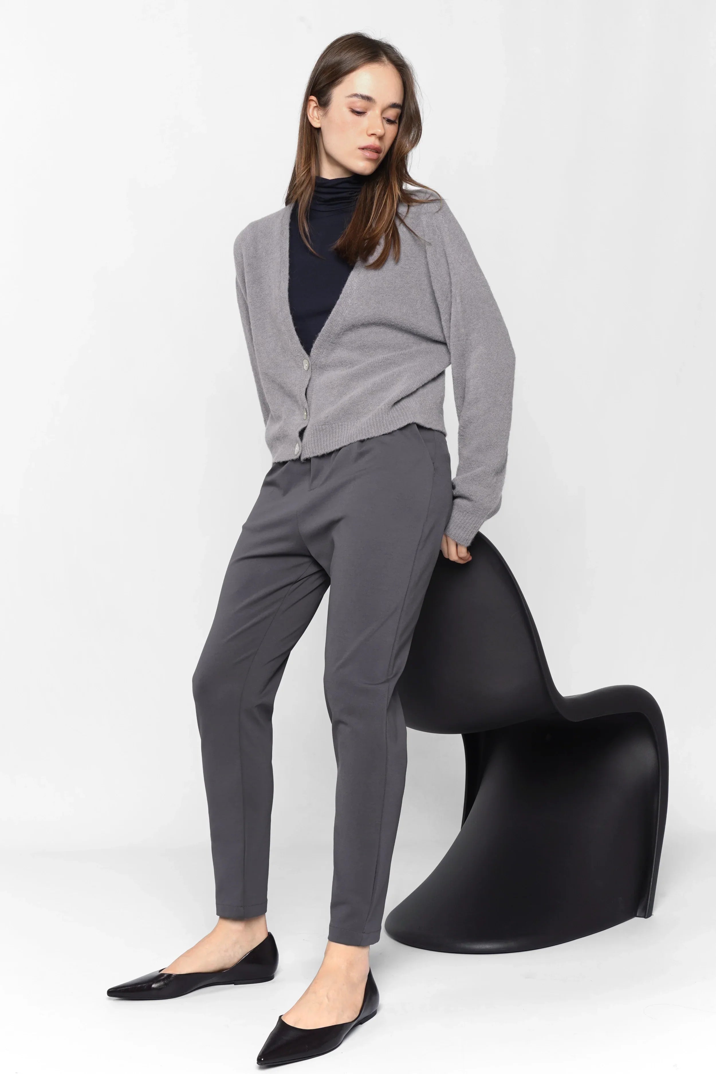 Woman wearing grey HEELENA Tapered Pants with cardigan and black flats, modern tapered fit, soft wrinkle-resistant fabric.