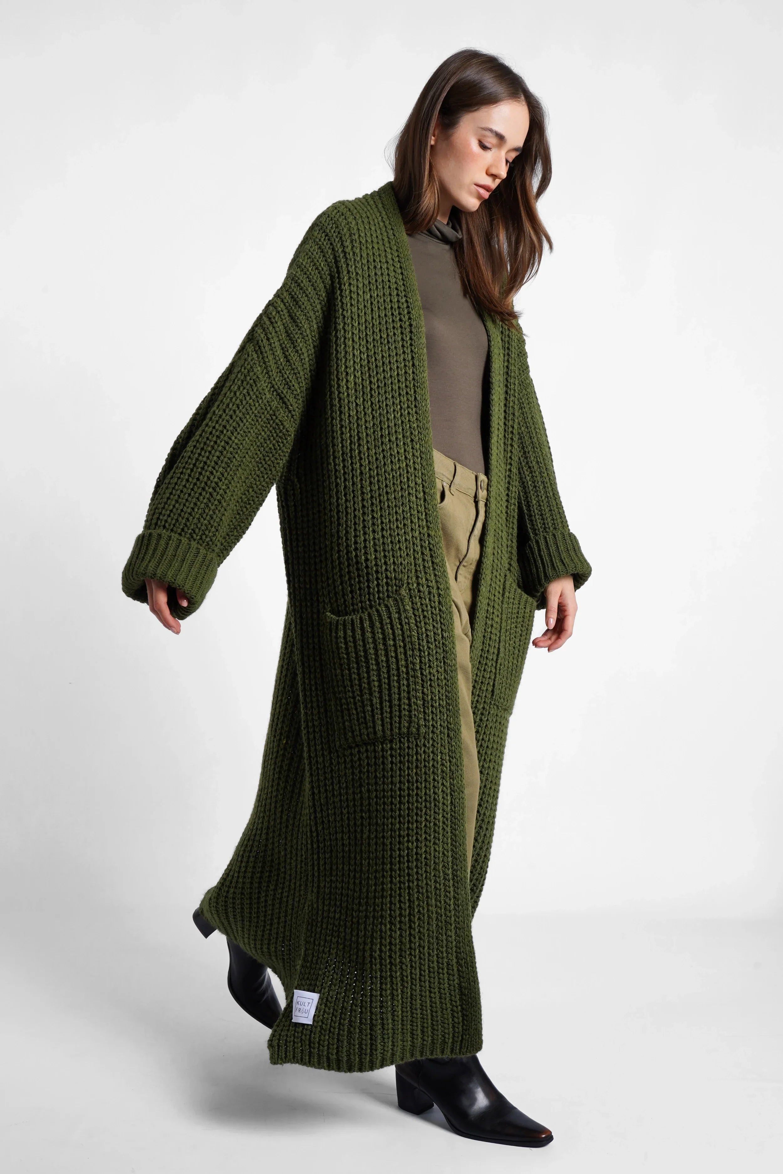 Frau trägt grünen LOLA Strickcardigan im Oversize-Schnitt mit aufgesetzten Taschen, locker und offen zum Tragen