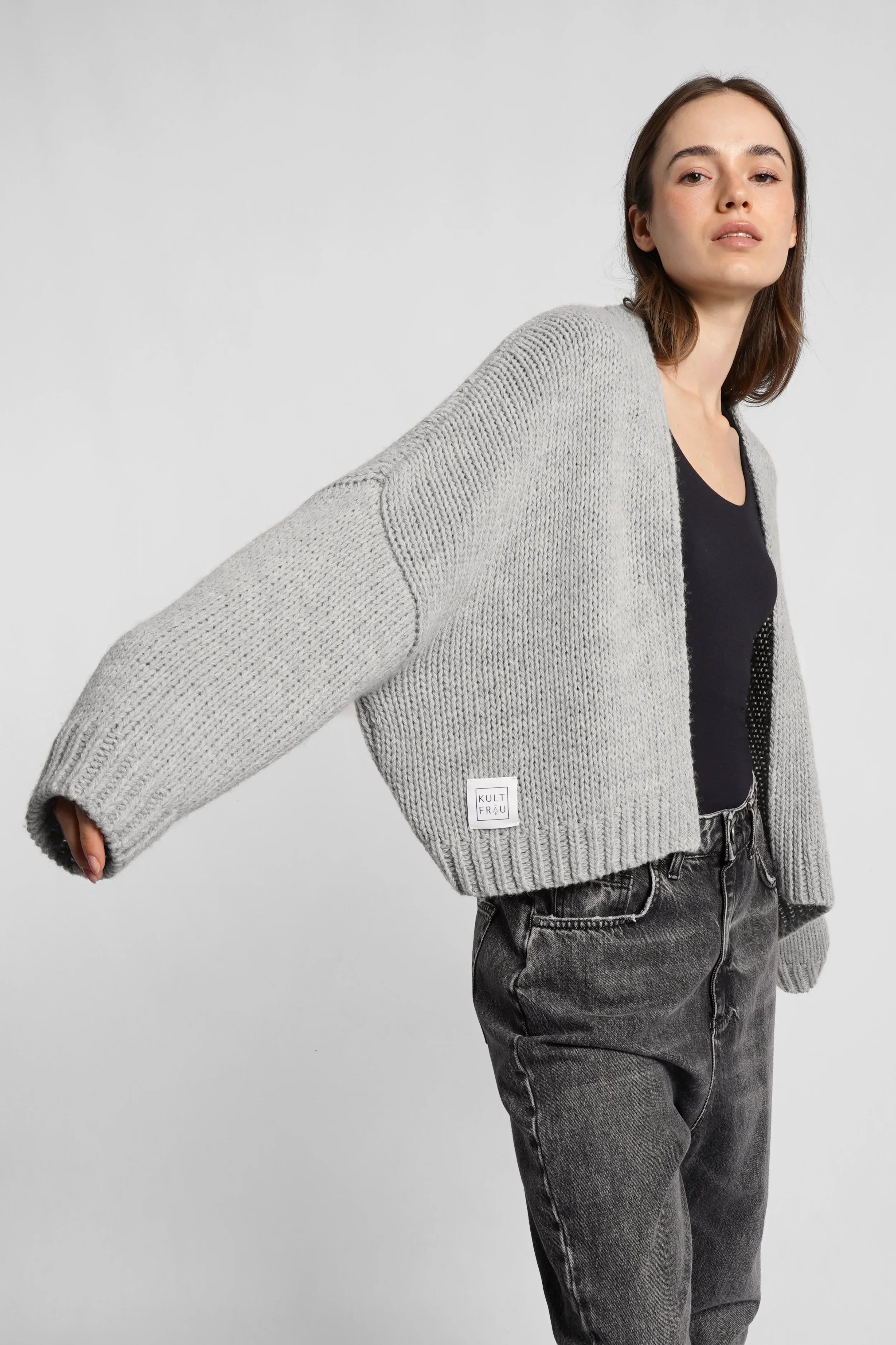 Woman wearing grey ALIXA Cropped Strickcardigan with shawl collar and loose fit over black top and jeans