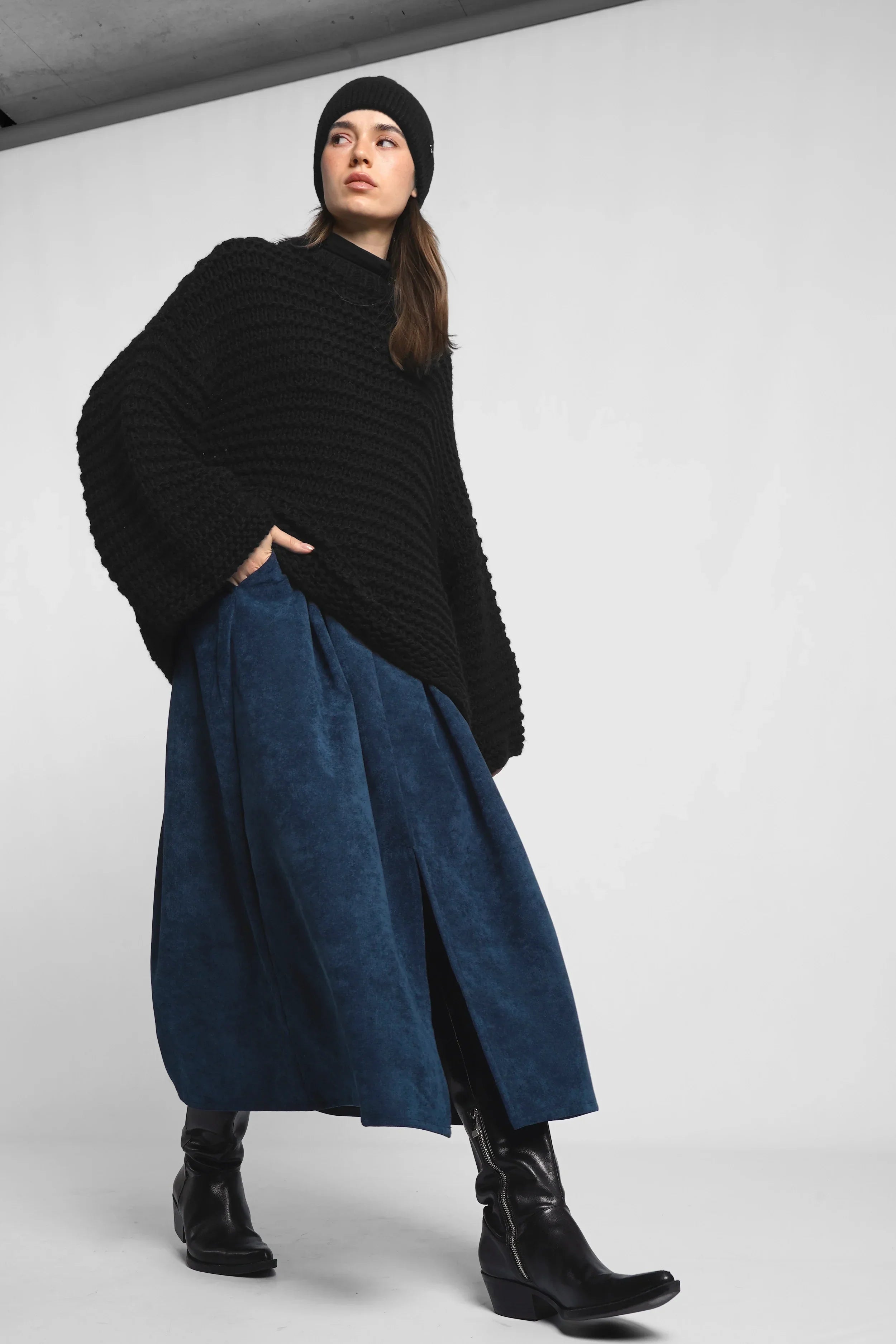 Woman wearing blue cord midi skirt with side pockets and front slit, black sweater and boots