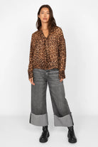 Woman wearing EDITHA Seidenbluse leopard print silk blouse with relaxed fit and puff sleeves paired with wide cuffed grey jeans and black boots.