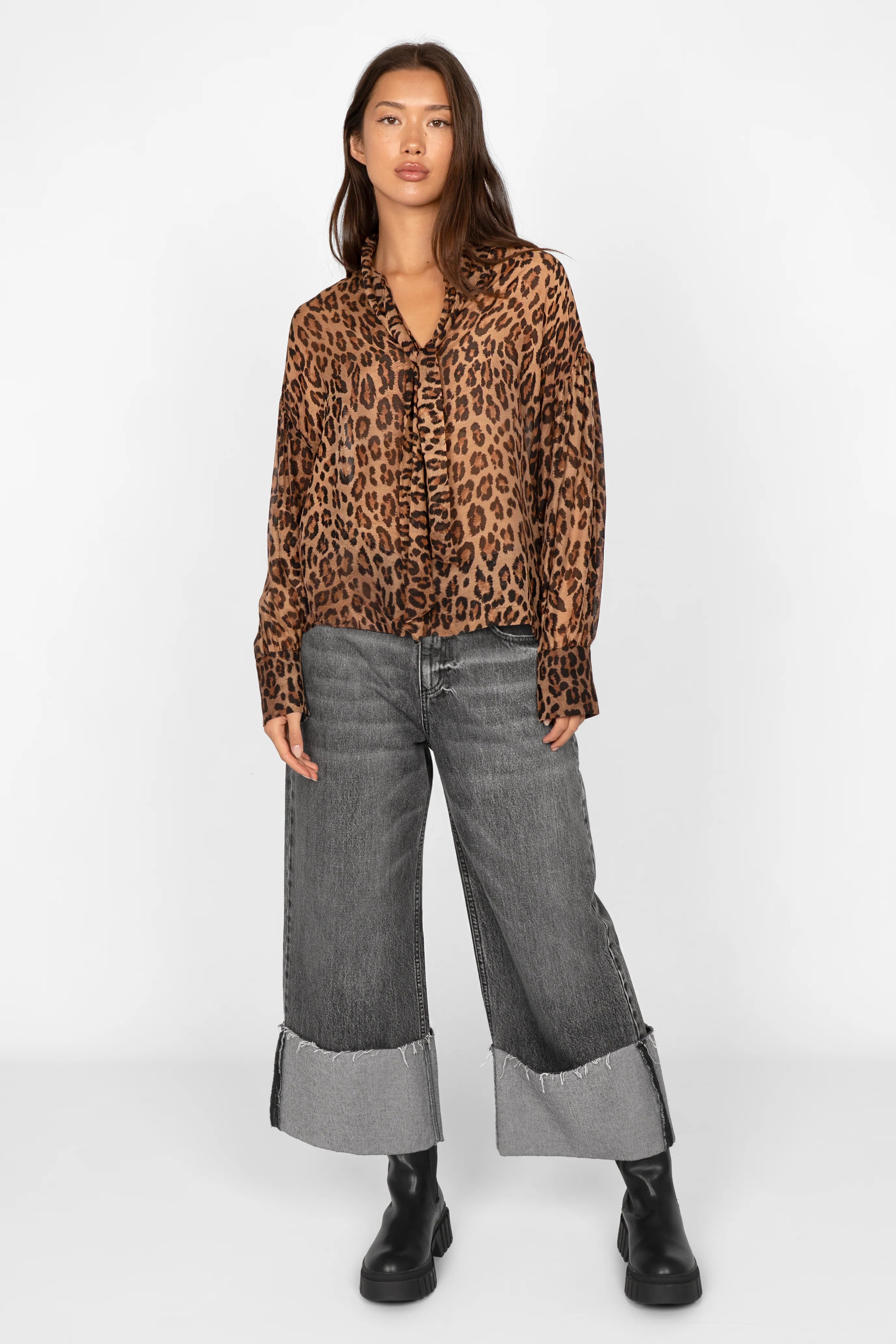 Woman wearing EDITHA Seidenbluse leopard print silk blouse with relaxed fit and puff sleeves paired with wide cuffed grey jeans and black boots.