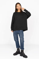 Schwarzer EIREL Oversize Sweater mit A-Linie, überschnittenen Schultern und tonaler Logo-Stickerei, kombiniert mit Jeans und schwarzen Boots