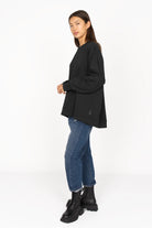 Schwarzer oversized Sweater mit gerader Silhouette, überschnittenen Schultern und tonaler Logo-Stickerei, kombiniert mit blauen Jeans und schwarzen Stiefeln.