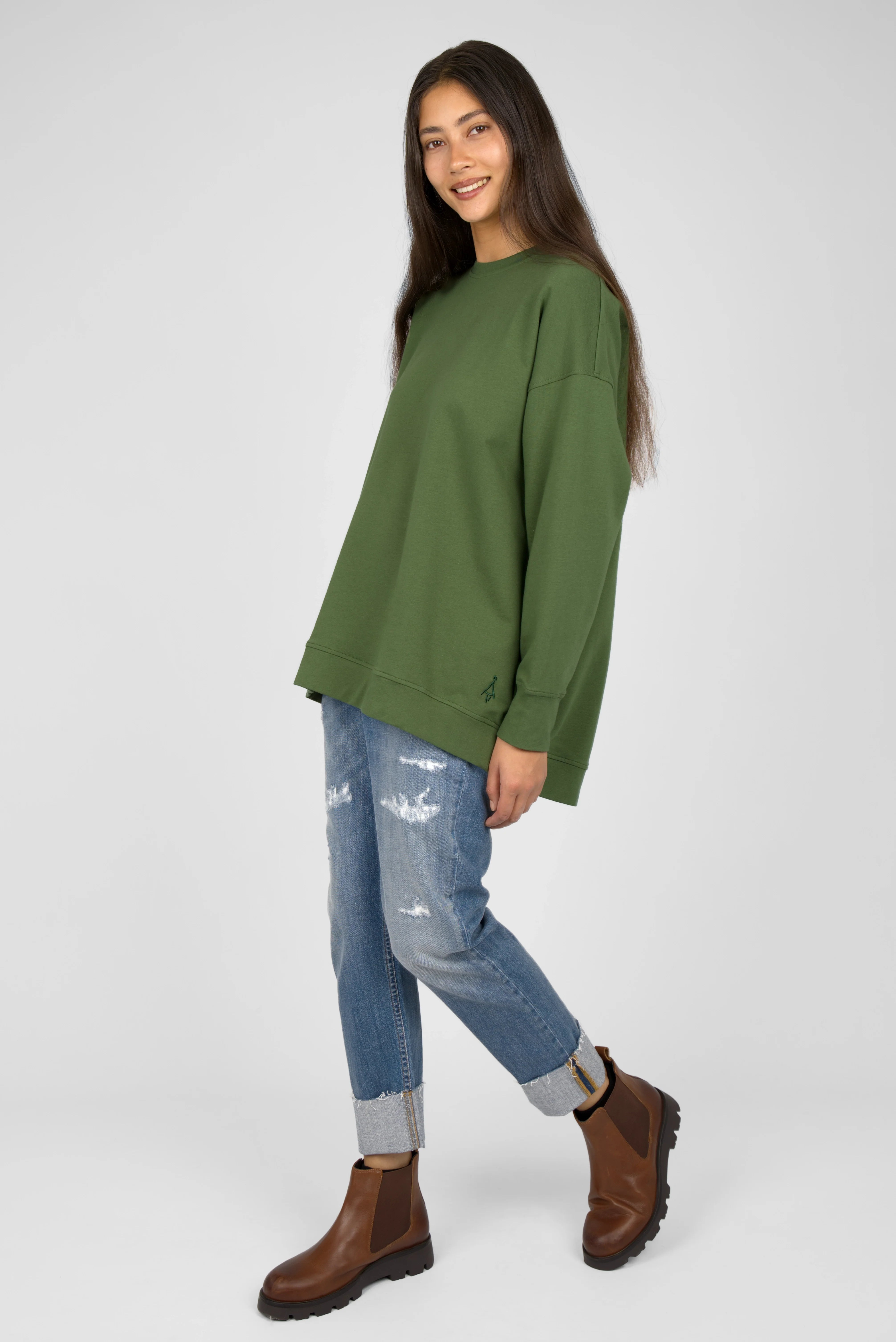Woman wearing green oversized sweater with dropped shoulders and tonal logo embroidery paired with rolled-up jeans and brown boots