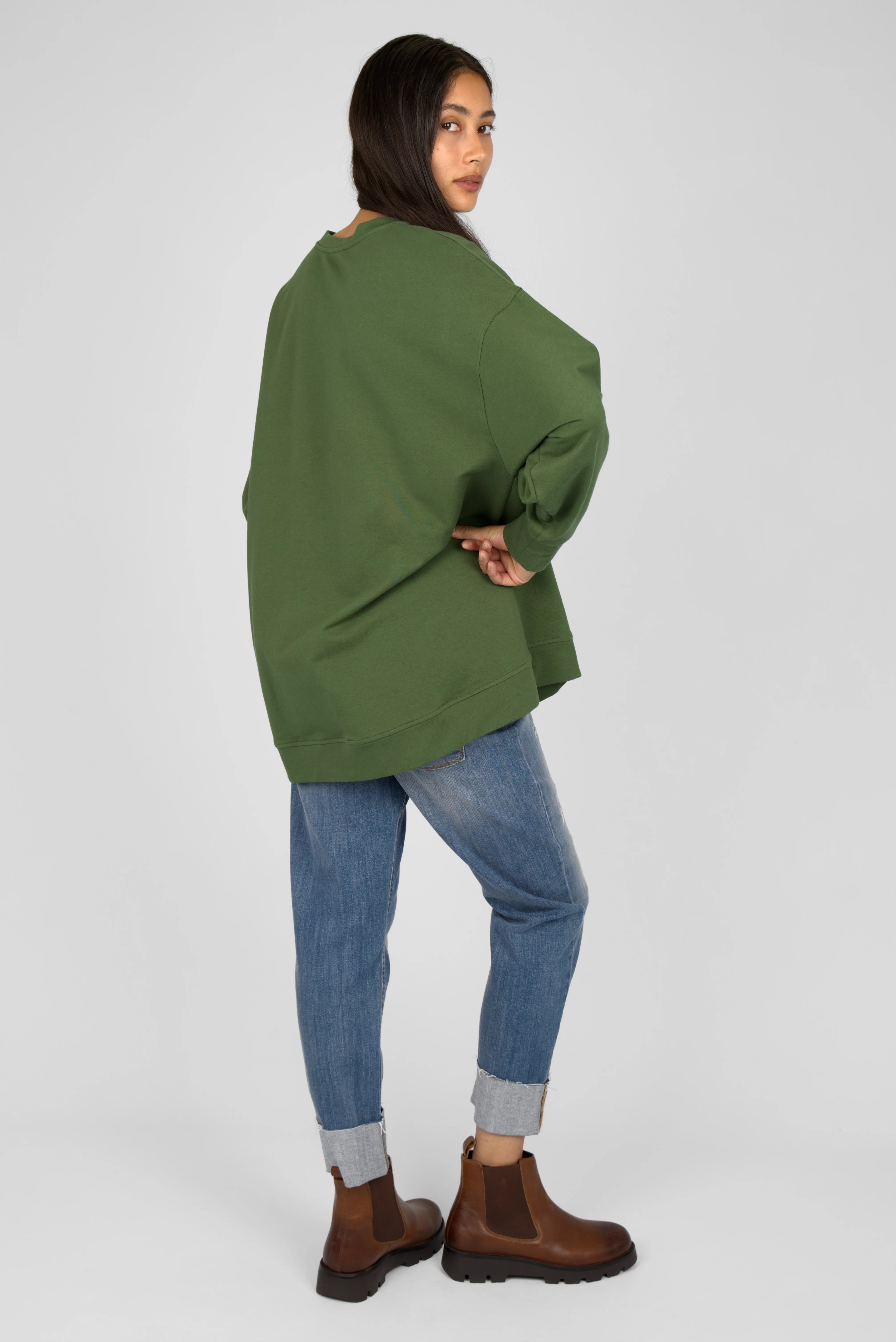 Woman wearing green EIREL oversize sweater with dropped shoulders and rounded hem, paired with cuffed jeans and brown ankle boots, shown from the back
