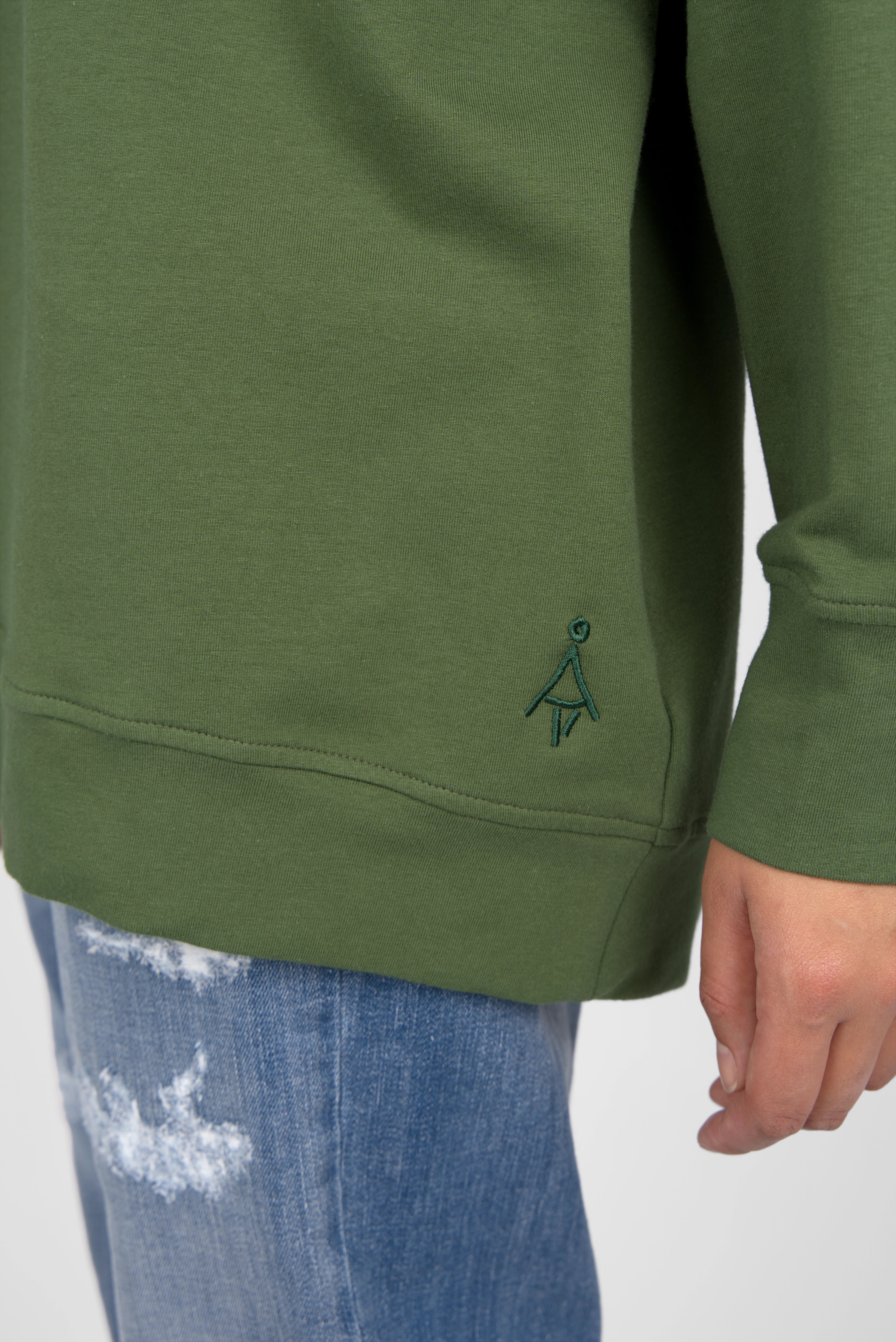 Green oversize sweater with tonal logo embroidery and elongated cuffs on model wearing distressed blue jeans