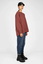 Woman wearing a rust-colored EIREL oversize sweater with dropped shoulders and relaxed fit paired with blue jeans and black boots
