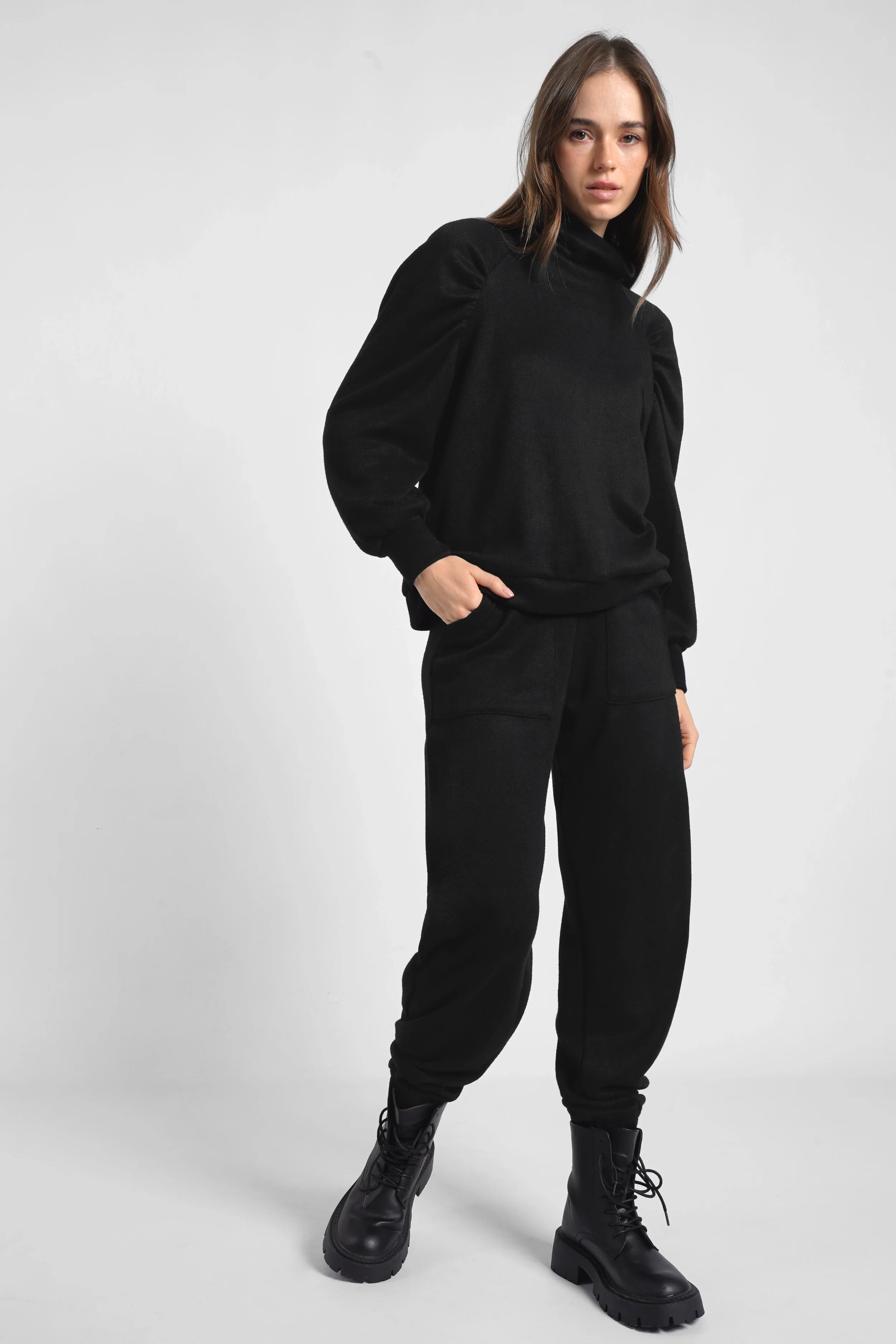 Woman wearing black FRELA Jogpant made of soft fine knit with elastic waistband and ribbed cuffs, styled with black boots and black top.