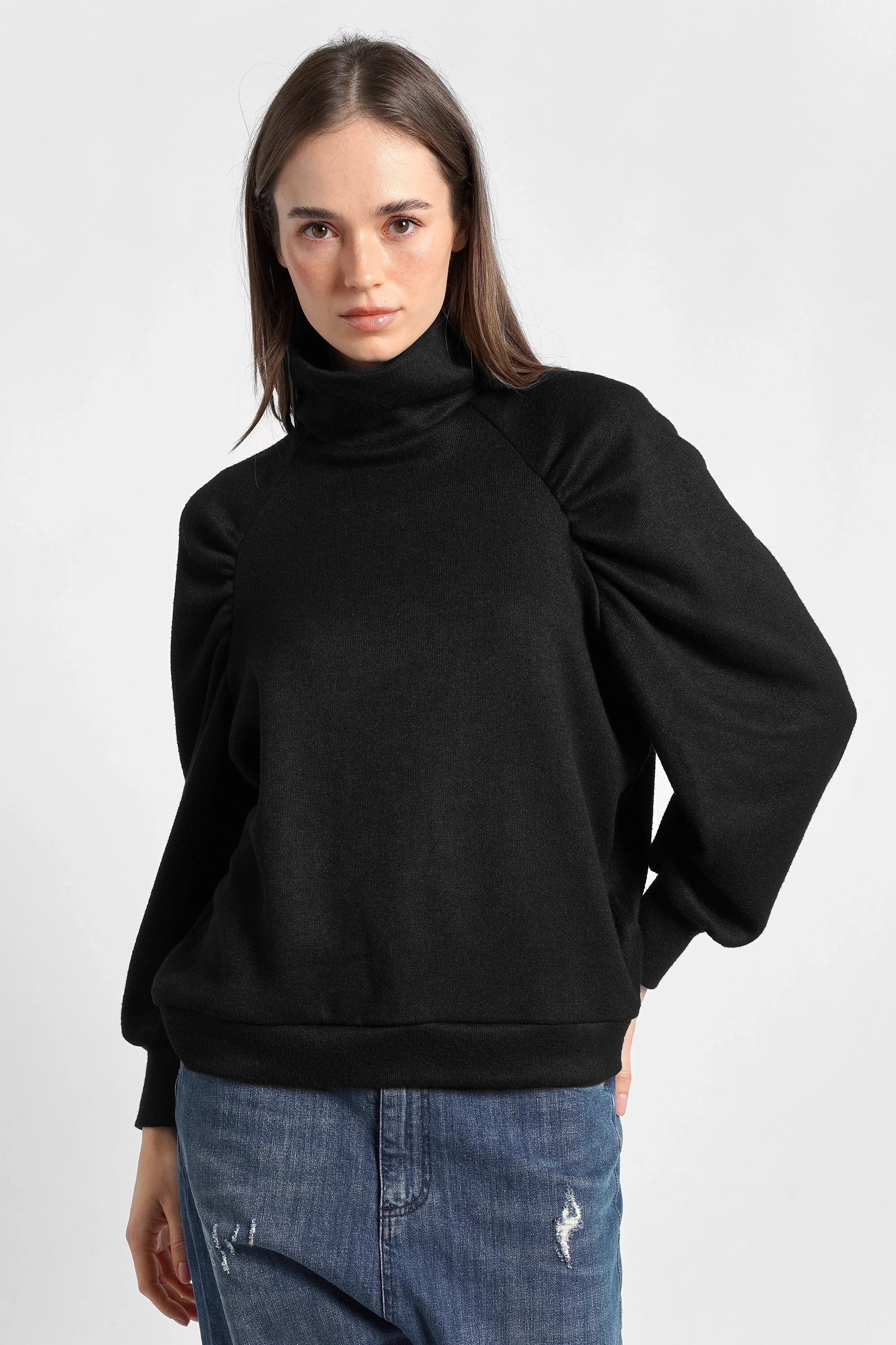 Frau trägt schwarzes Oberteil aus softem Feinstrick mit Stehkragen und Raglanärmeln.