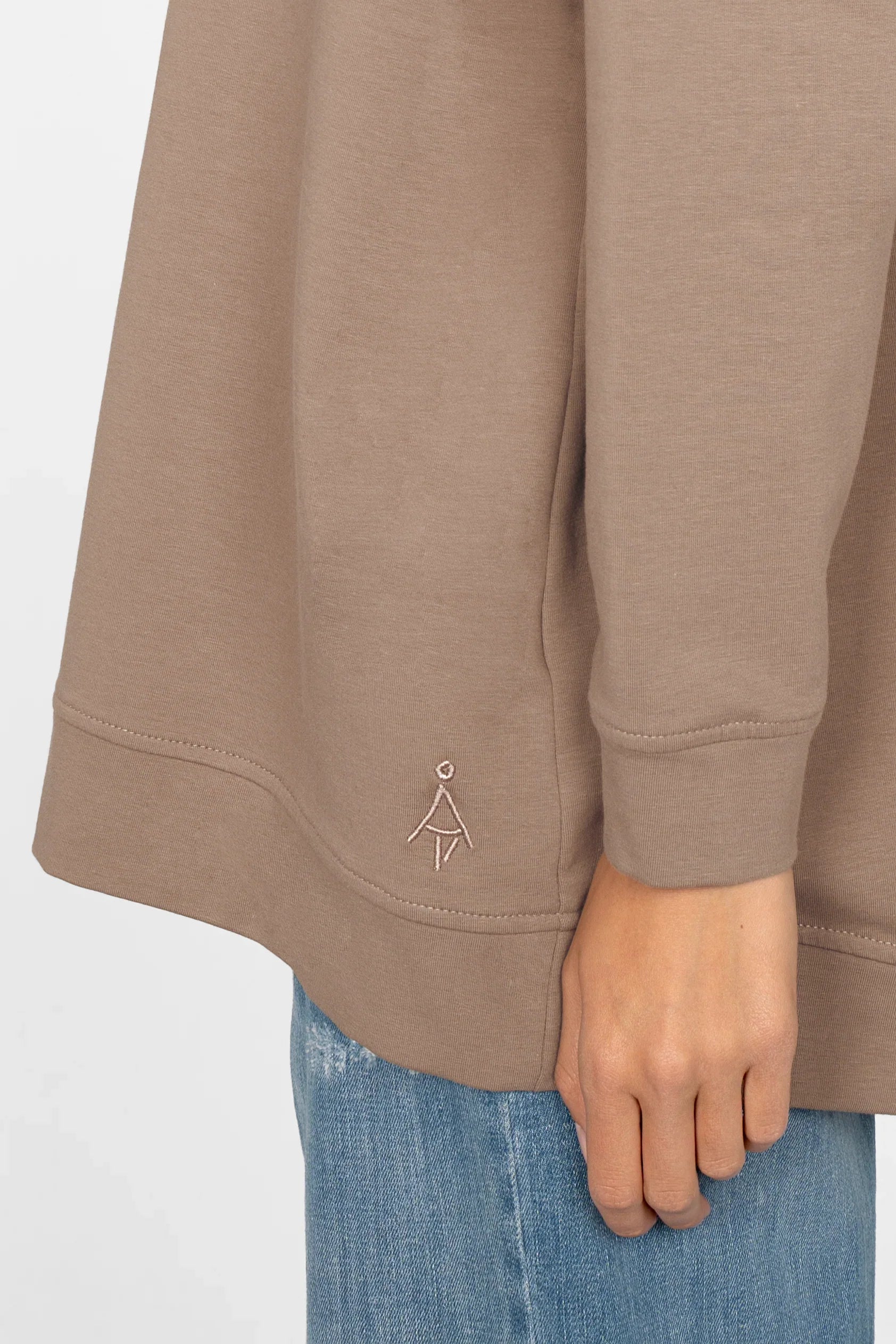 Close-up of beige GRACEY.K Sweater with tonal logo embroidery and rounded hem on model wearing blue jeans