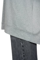 Close-up of grey GRACEY.K Sweater with tonal logo embroidery and rounded hem over dark denim jeans