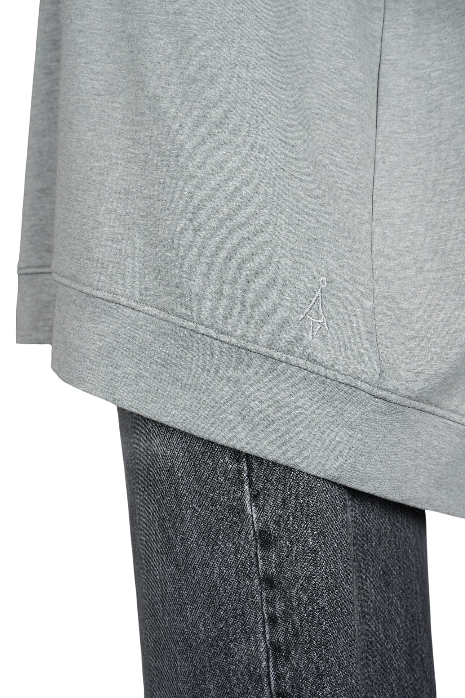 Close-up of grey GRACEY.K Sweater with tonal logo embroidery and rounded hem over dark denim jeans