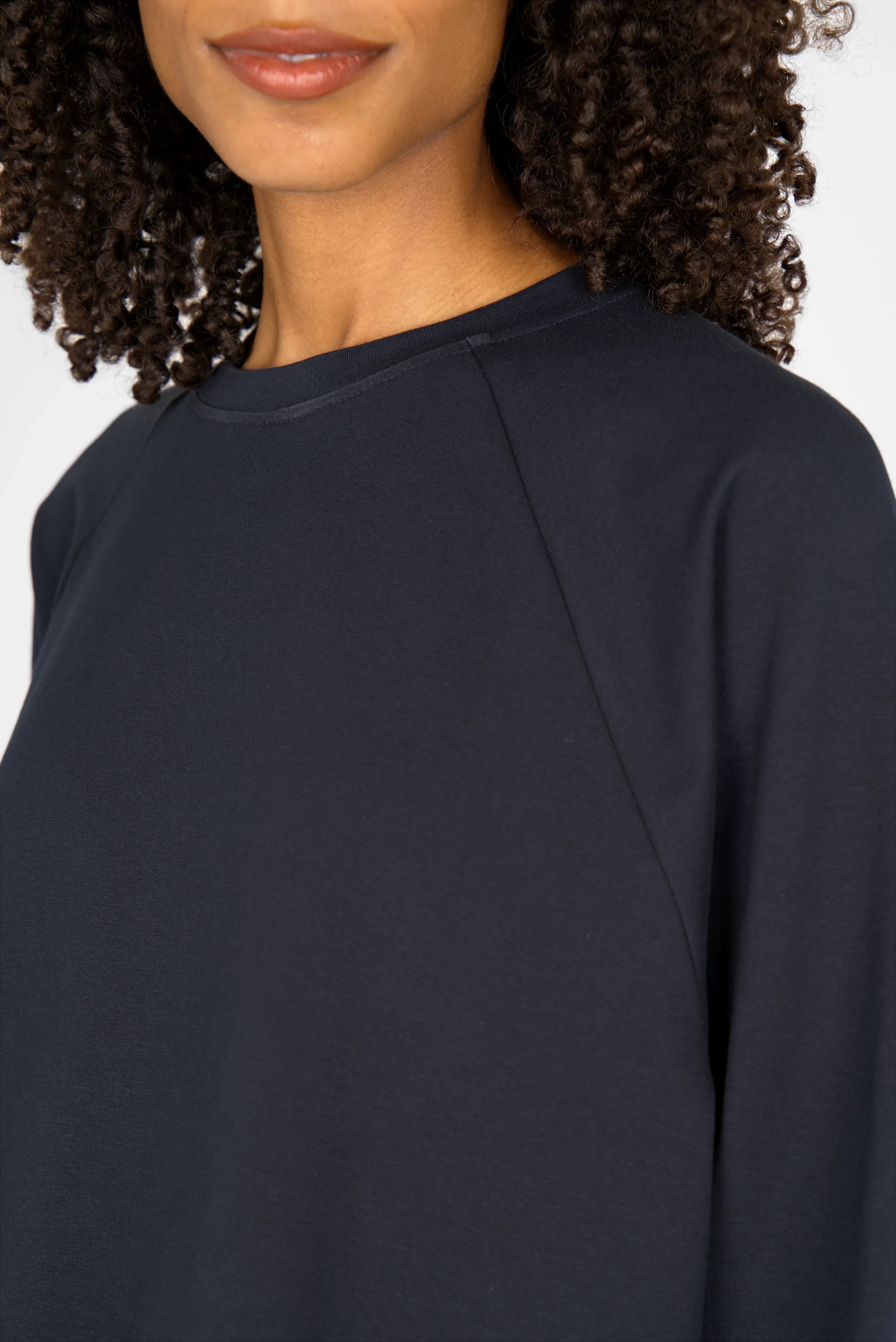Close-up of woman wearing navy GRACEY.K Sweater with raglan sleeves and round neckline, showing soft fabric and subtle tonal logo embroidery