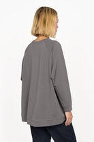 Back view of a model wearing a grey GRACEY.K Sweater with an oversized fit and longer A-line hem.