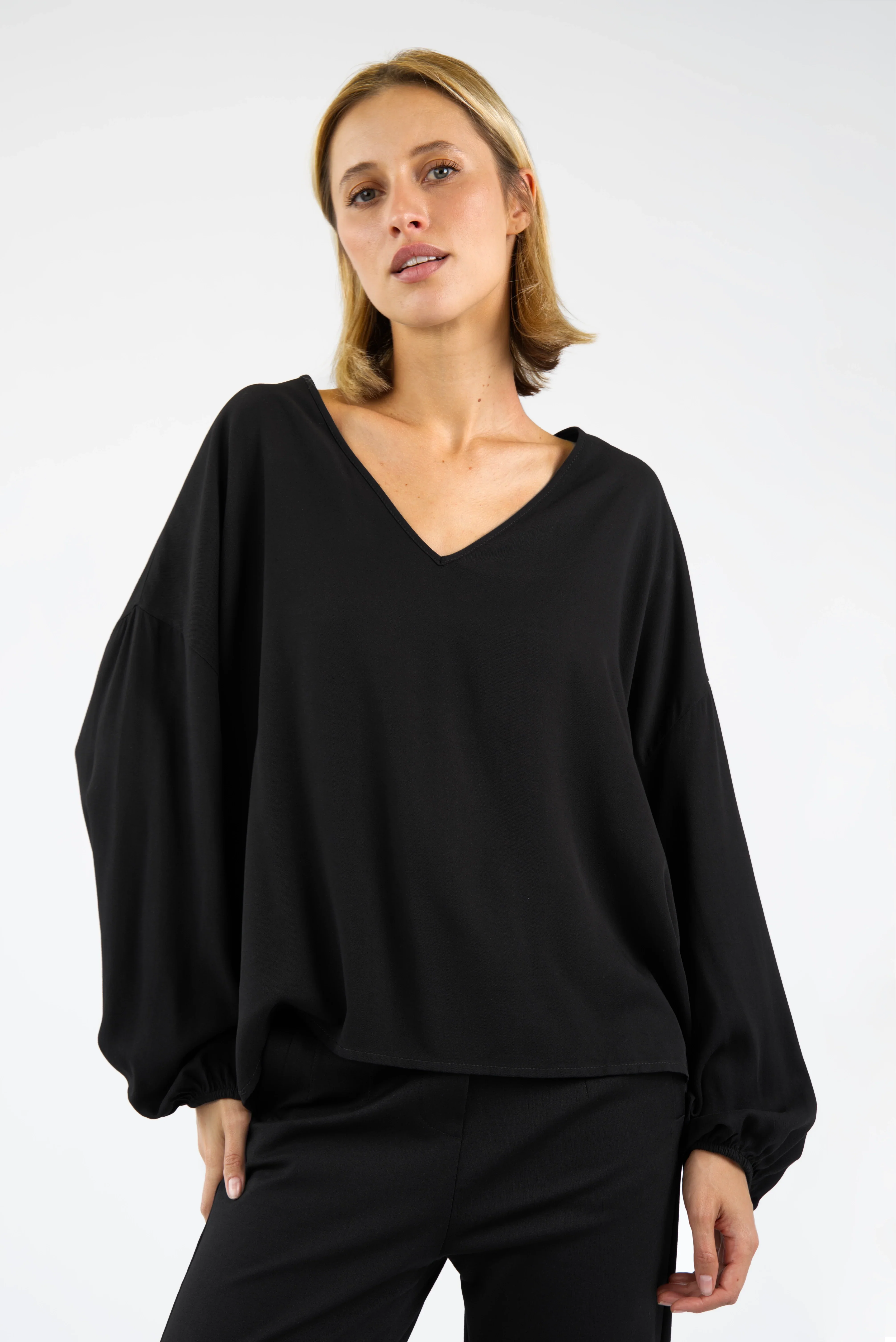 Woman wearing GRETA.K V-Neck Bluse black relaxed fit blouse with long elastic sleeves and dropped shoulders
