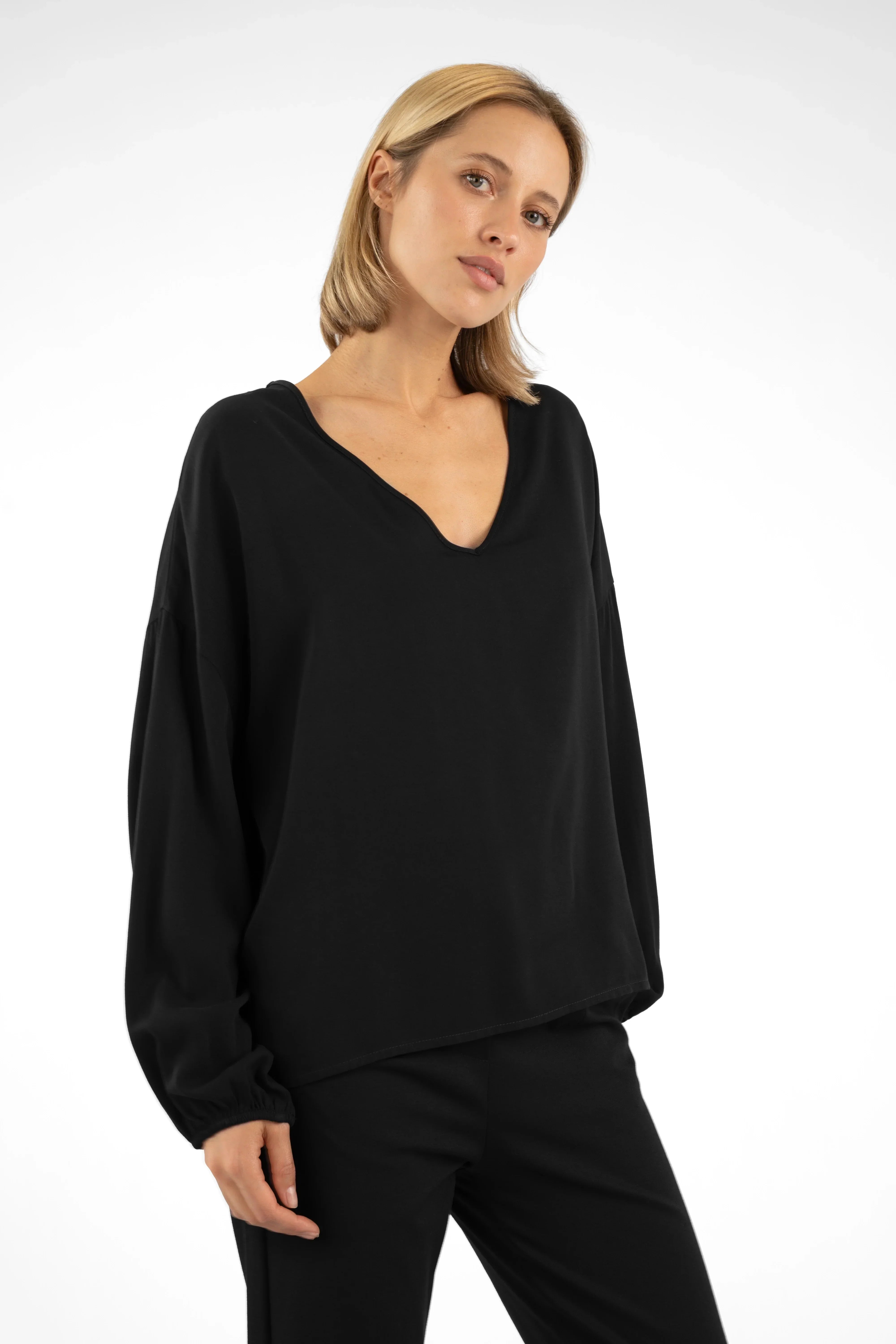 Frau trägt lockere schwarze GRETA.K V-Neck Bluse aus weicher Twill Viskose mit überschnittenen Schultern und elastischen Ärmeln