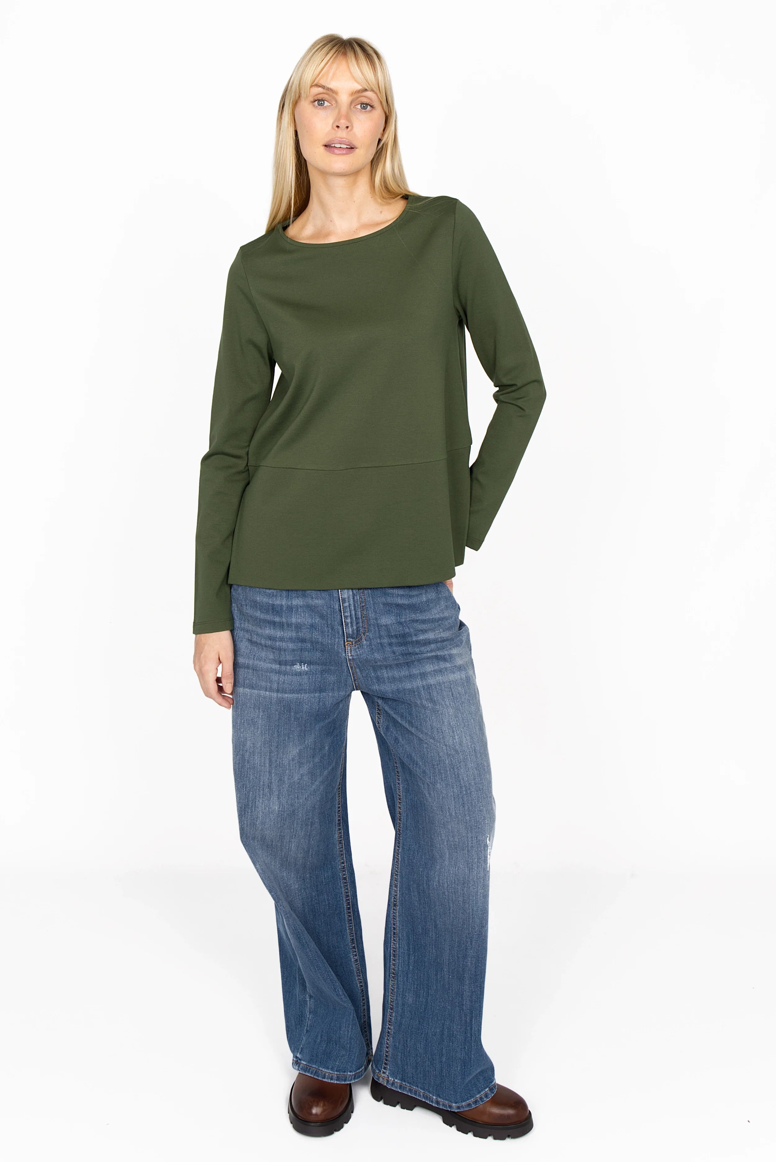 Female model wearing olive green HAEIN Clean Jersey long sleeve top with U-boat neckline and side slits paired with blue wide-leg jeans