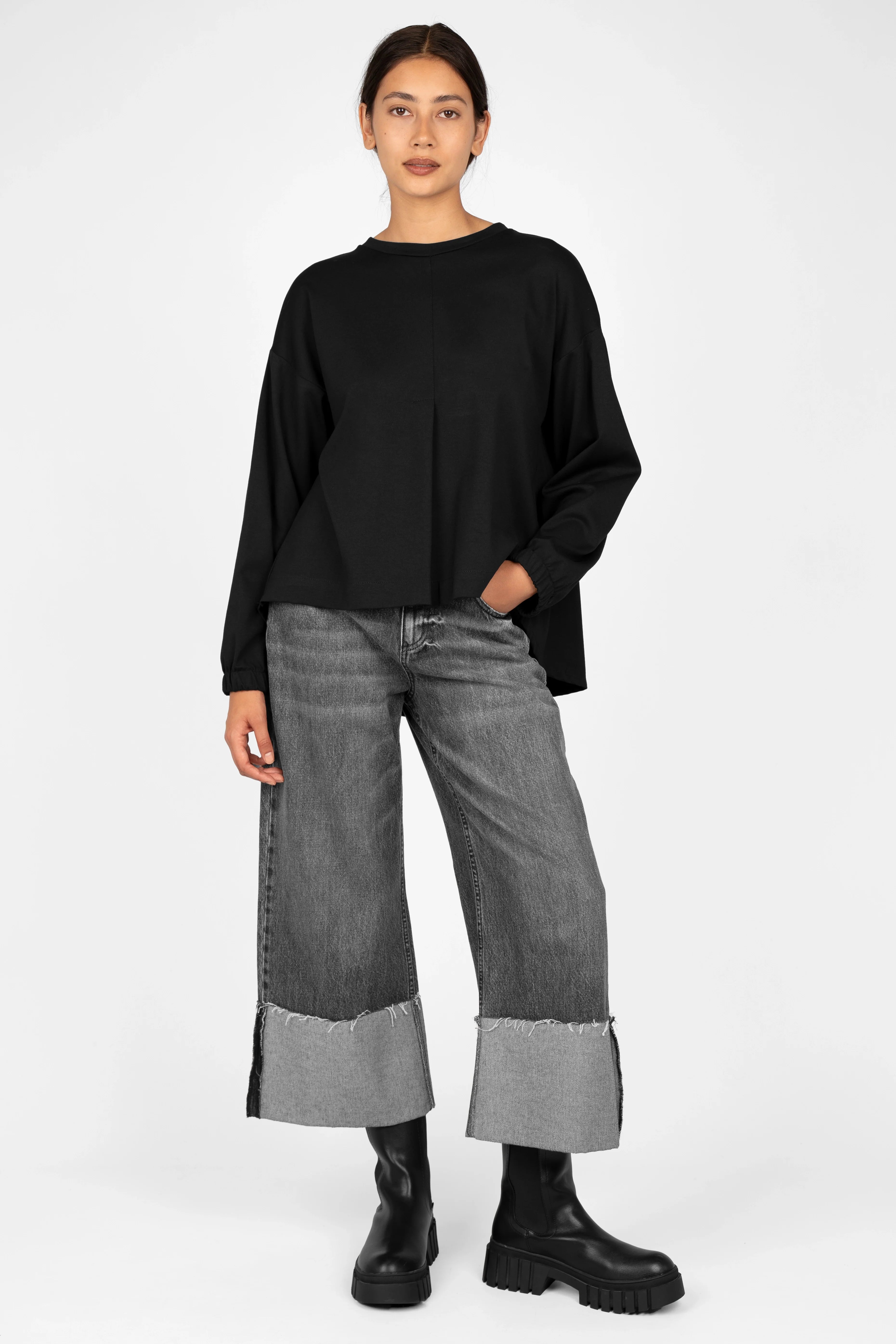 Black HAGLA Shirt in relaxed fit with round neckline, elastic cuffs, and back pleat detail worn with gray cuffed jeans and black boots