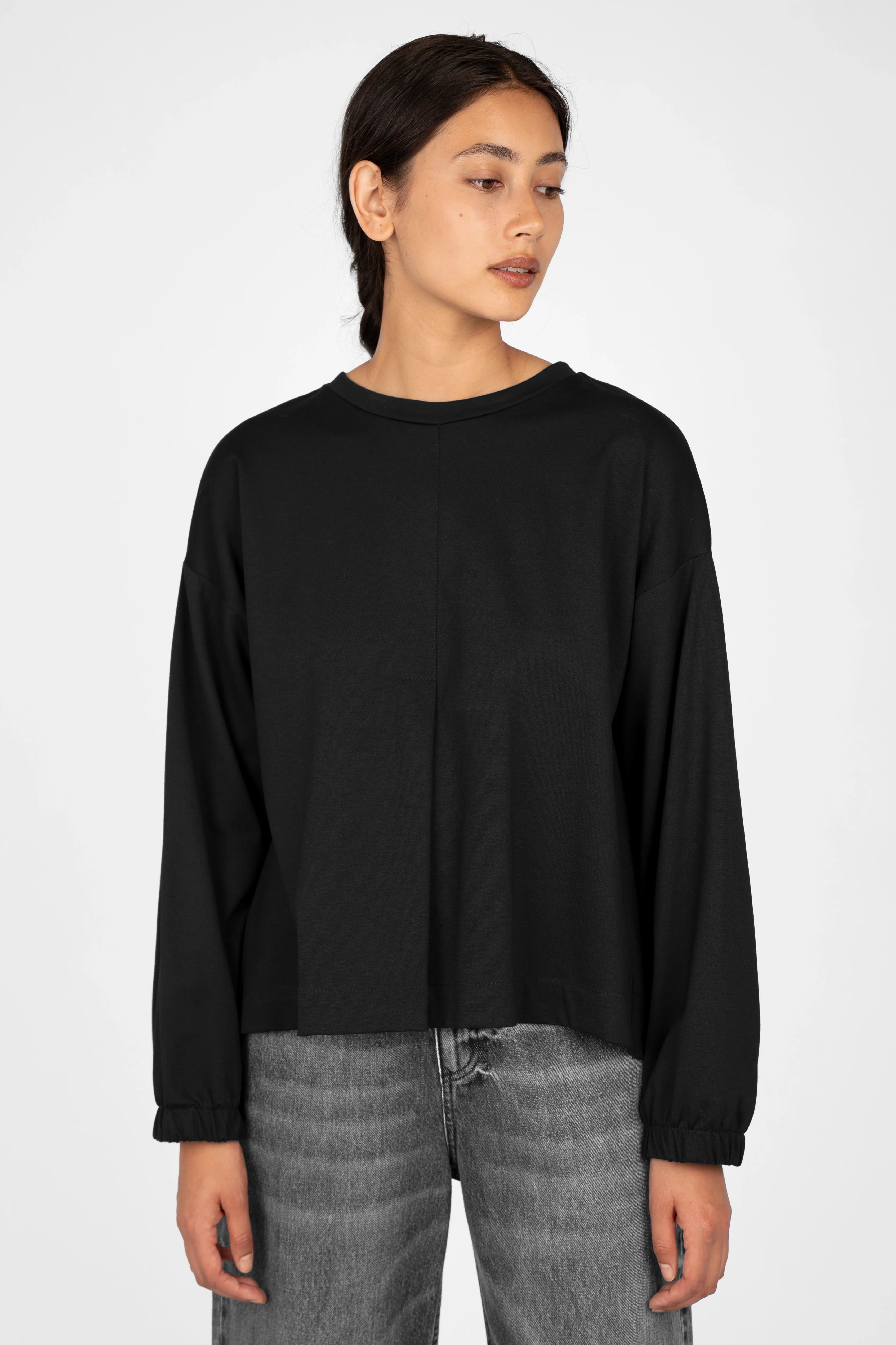 Black HAGLA Shirt with relaxed fit, round neckline, elastic cuffs, and subtle front and back pleats, worn by a female model.