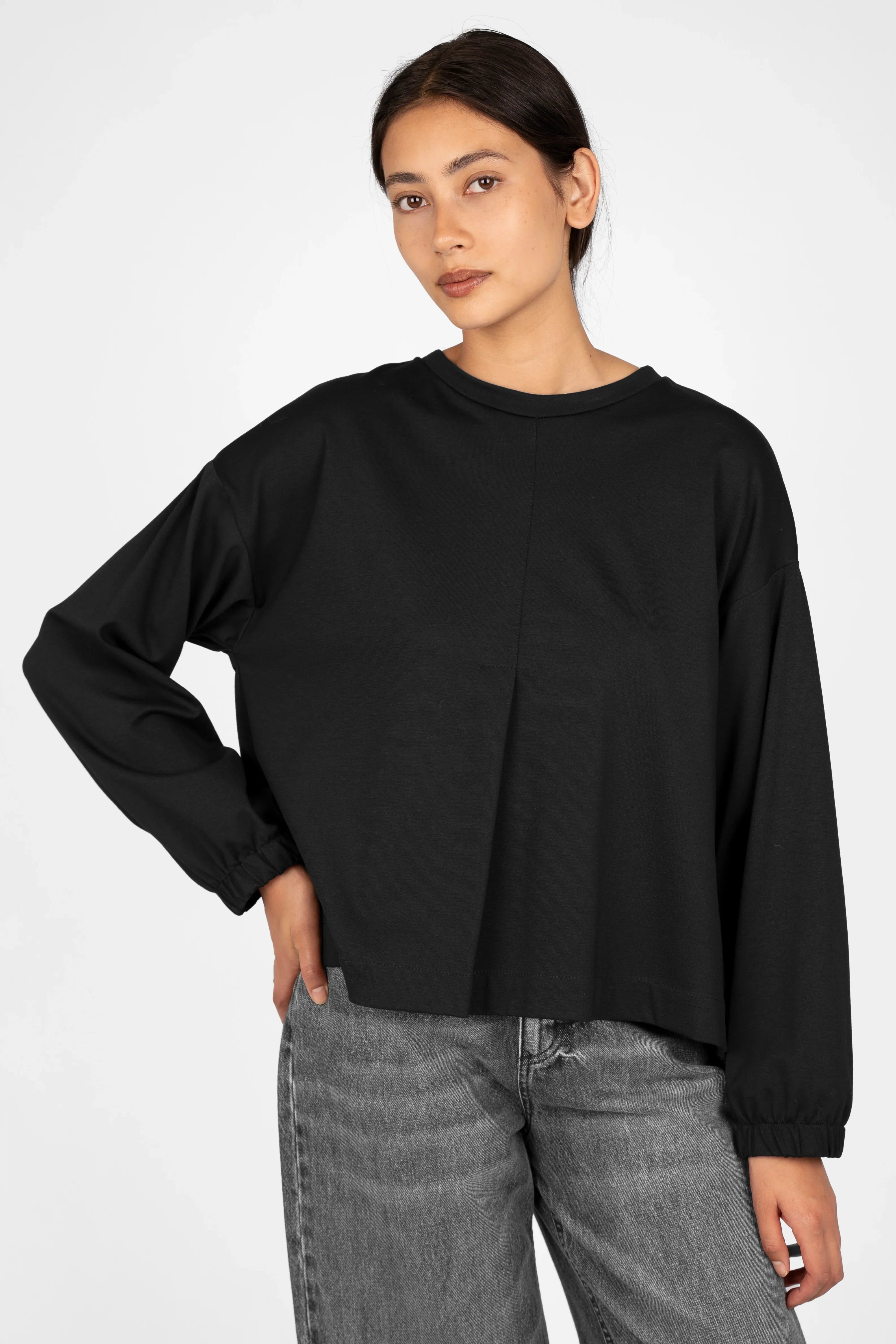 Frau trägt schwarzes HAGLA Shirt aus Heavy Viskose-Mix mit Rundhalsausschnitt, elastischen Bündchen und Rückenfalte, Relaxed Fit, vorne kürzer als hinten.