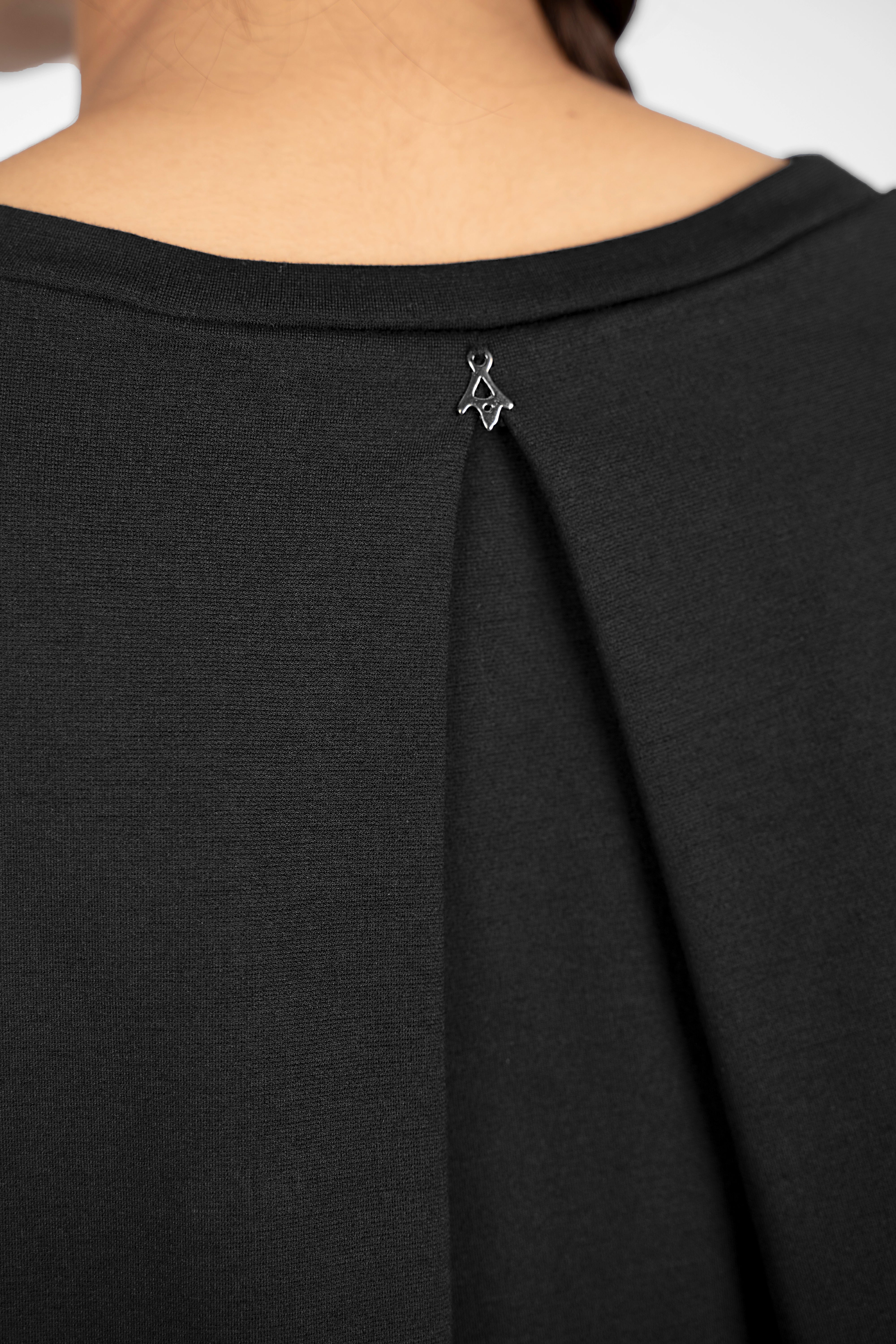 Close-up of black HAGLA Shirt showing back pleat detail and small metal logo near neckline
