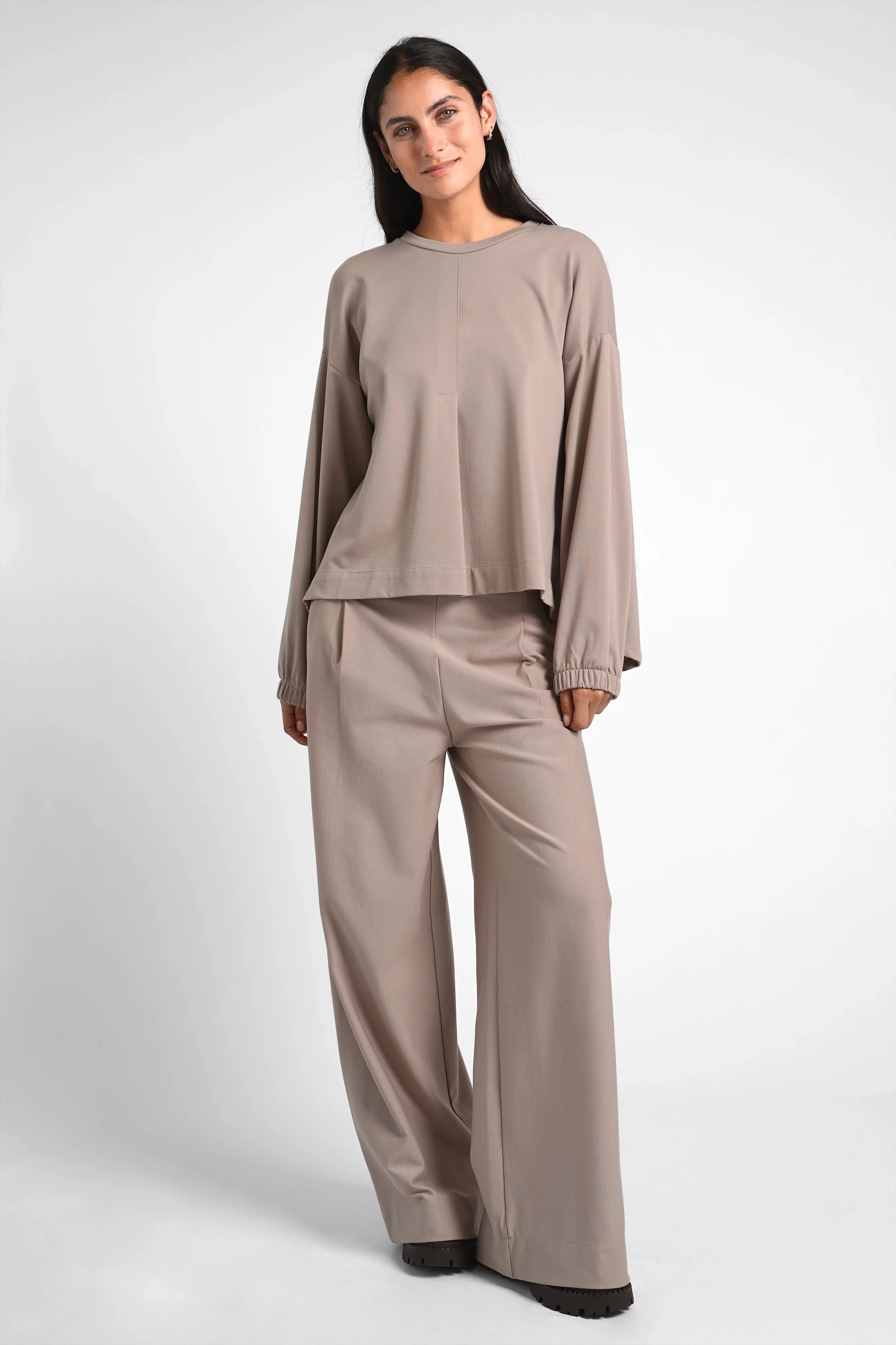 Woman wearing taupe HAGLA Shirt with round neckline, elastic cuffs, and relaxed fit paired with matching wide-leg pants