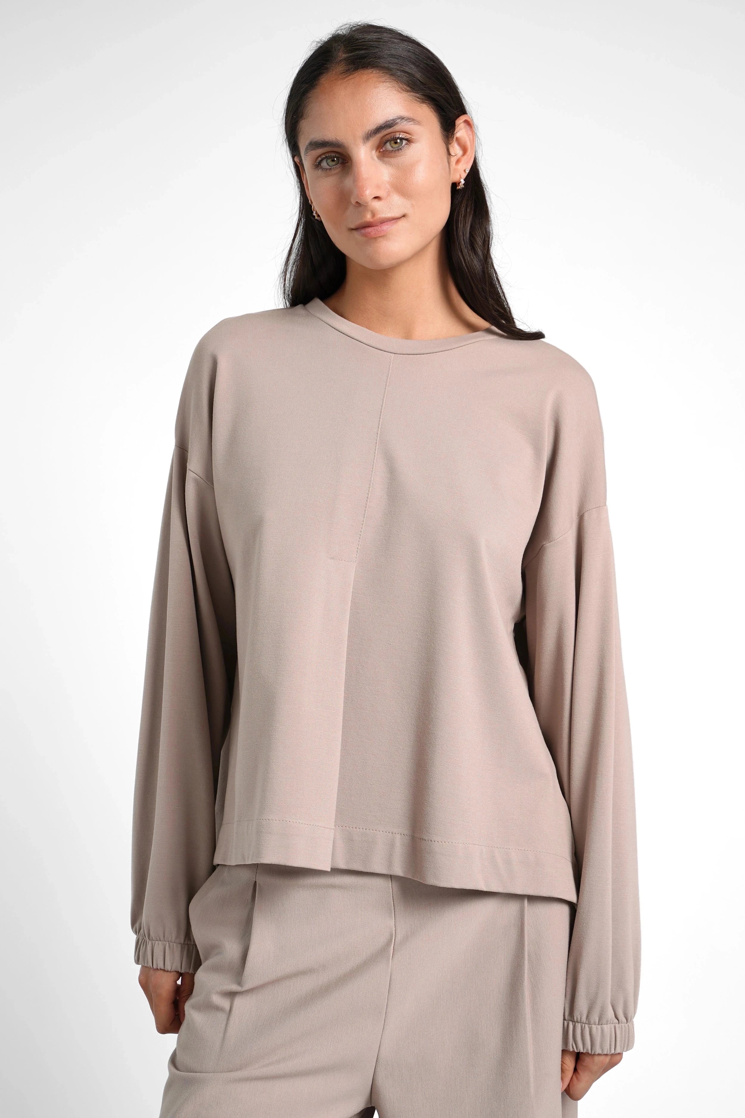 Woman wearing beige HAGLA Shirt with round neckline, elastic cuffs, and relaxed fit against white background