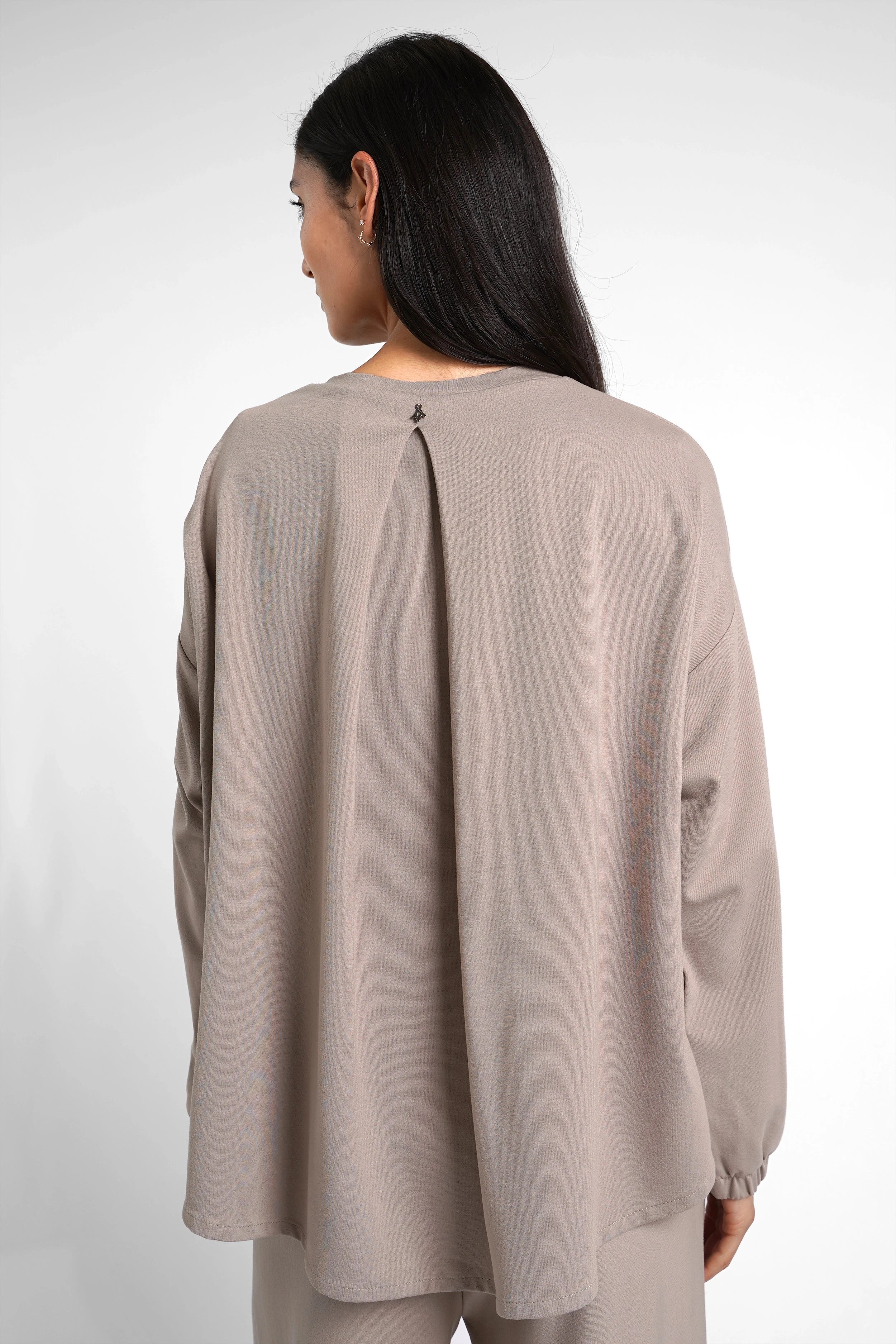 Back view of a woman wearing a loose-fitting, beige HAGLA Shirt with a pleat detail and elastic cuffs made from heavy viscose blend