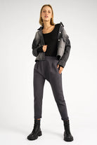 Damen in schwarzer HANNA.K Tapered Sweathose mit elastischem Bund, tiefem Schritt und schmal zulaufendem Bein, kombiniert mit schwarzem Top und grauer Jacke.